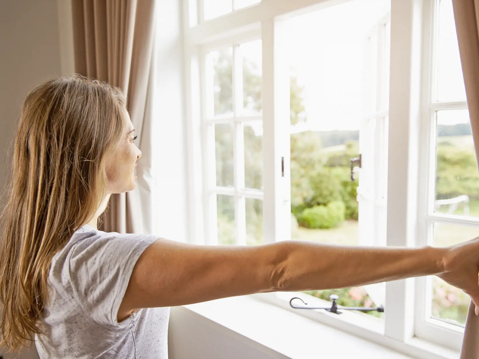Woman,Standing,By,Bedroom,Window,And,Opening,Curtains