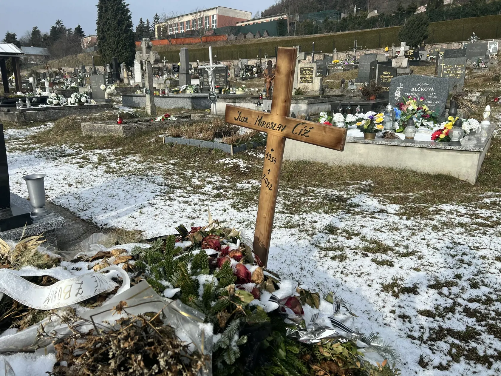 Namiesto pomníka tu dočasne stojí len jednoduchý drevený kríž a hrob pôsobí ako keby sa oň nik nestaral - ležia na ňom staré kvety ešte od pohrebu.