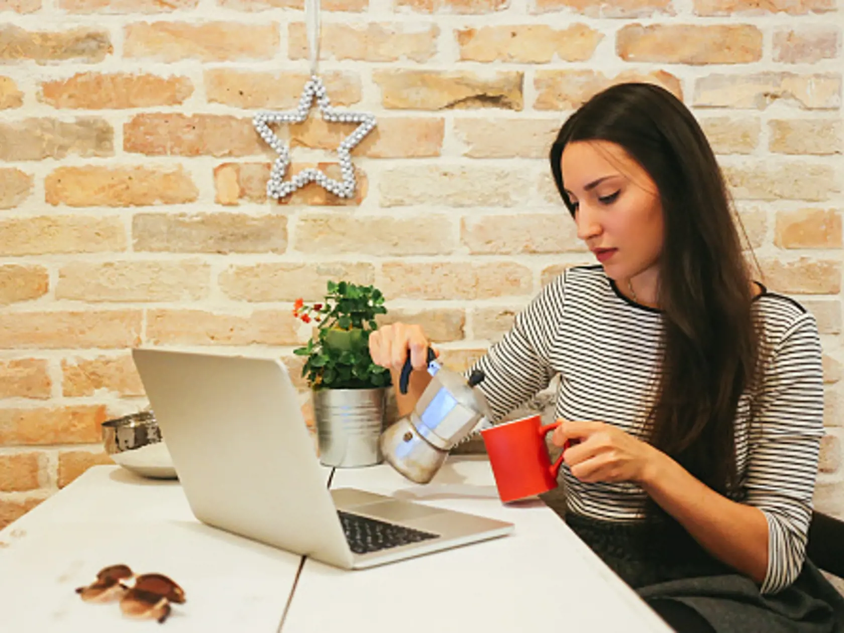 Vintage warm toned image of a young female novelist or a blogger, typing on the laptop keyboard in her bright apartment or an office space, sitting on the chair behind the desk. She's having a cup of hot coffee or tea while she's working or just browsing the web. Lifestyle - freelancer work concept in a casual environment.