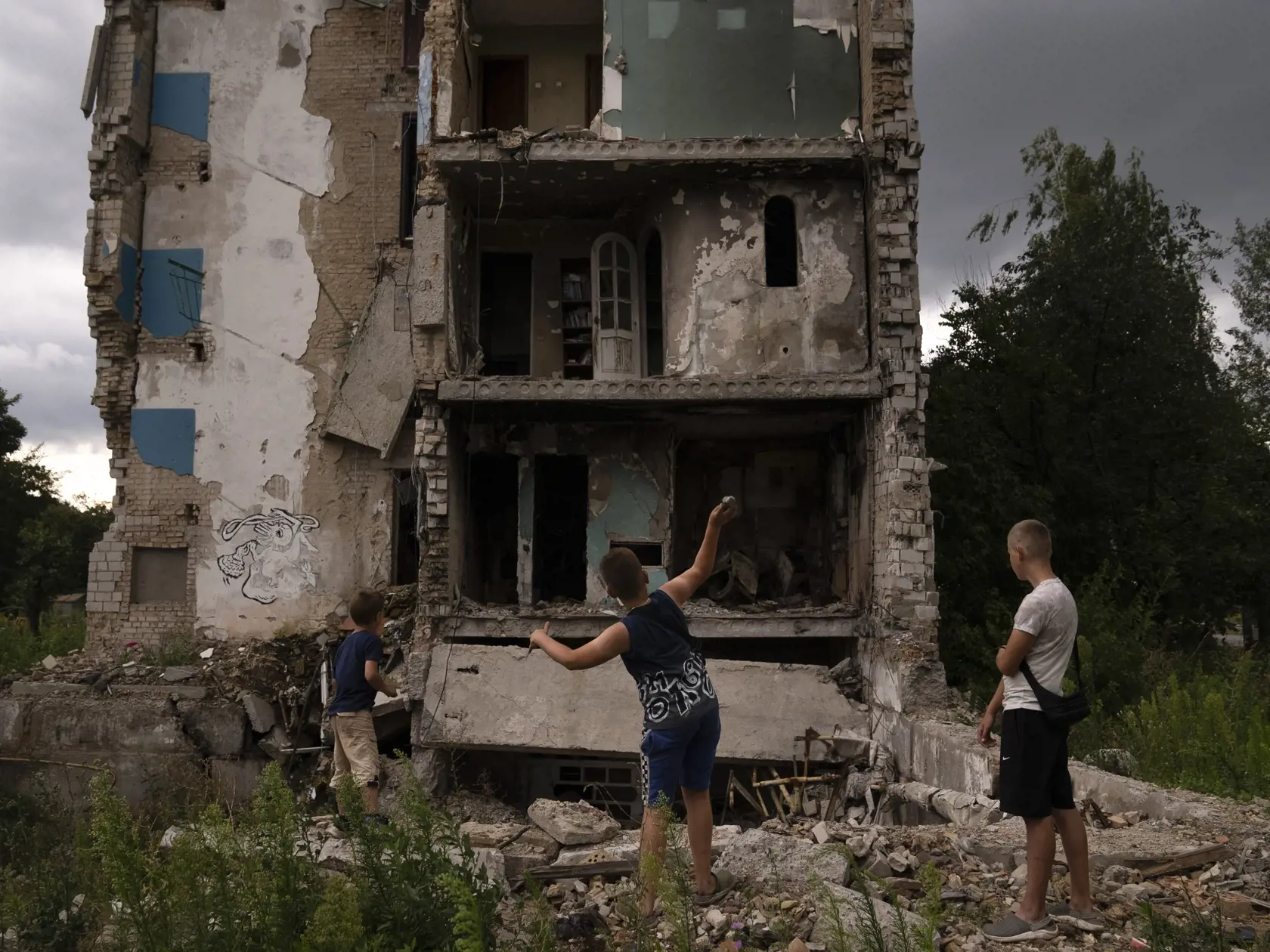 Na archívnej snímke z 2. augusta 2023 deti hádžu kamene do obytnej budoby zničenej po ruskom útoku v ukrajinskom meste Boroďanka.