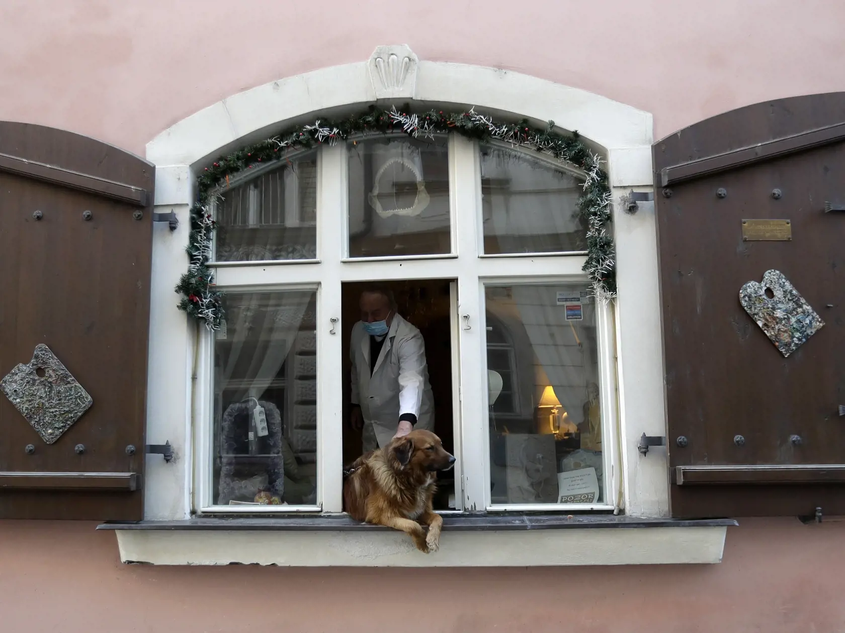 KK27 Praha - Muž hladká psa, ktorý sa pozerá z okna v Prahe 24. marca 2020.  Česko eviduje 1394 ľudí nakazených novým koronavírusom, počas utorka pribudlo viac ako 100 infikovaných. FOTO TASR/AP
A man pets a dog that sits in a window in Prague, Czech Republic, Tuesday, March 24, 2020.  The Czech government extended Monday its strict restrictions on movement of people and other activities until at least April 1 in efforts to contain the outbreak of the new coronavirus.  The highly contagious COVI