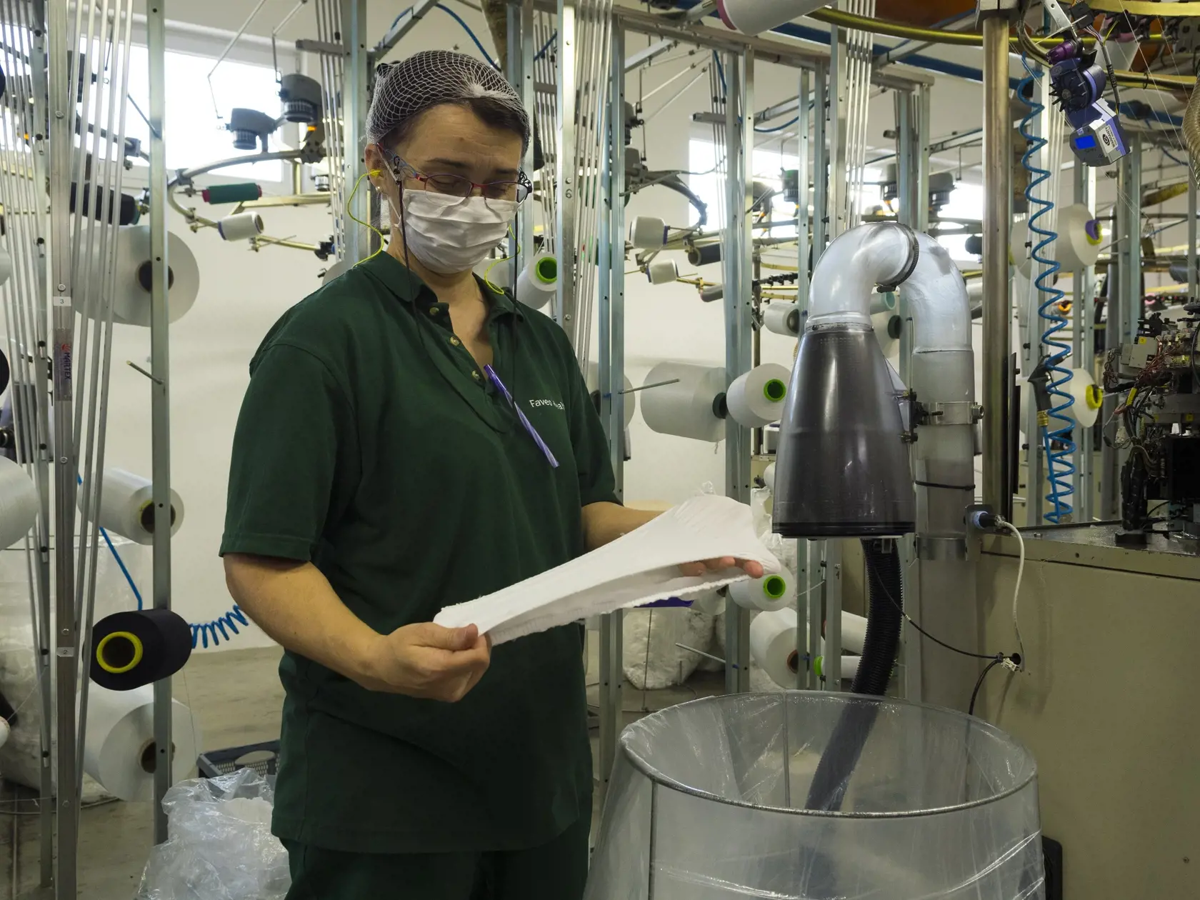 Spoločnosť Faveo Healthcare s.r.o Vranov nad Topľou sa špecializuje na výrobu zdravotníckeho materiálu. V spolupráci s firmou Chemosvit Fibrochem s.r.o. Svit vyvinuli vlastný vzor navliekacieho rúška. Aj keď denne vyrobia cca 6000 ks rúšok, nestíhajú naplniť ich dopyt. Na výrobu, ktorá plne automatizovaná, totiž vyčleňujú len voľné kapacity popri ich hlavnej výrobe. Na snímke vizuálna kontrola elastického rúška. Vranov nad Topľou, 2. apríla 2020. FOTO TASR – Milan Kapusta
