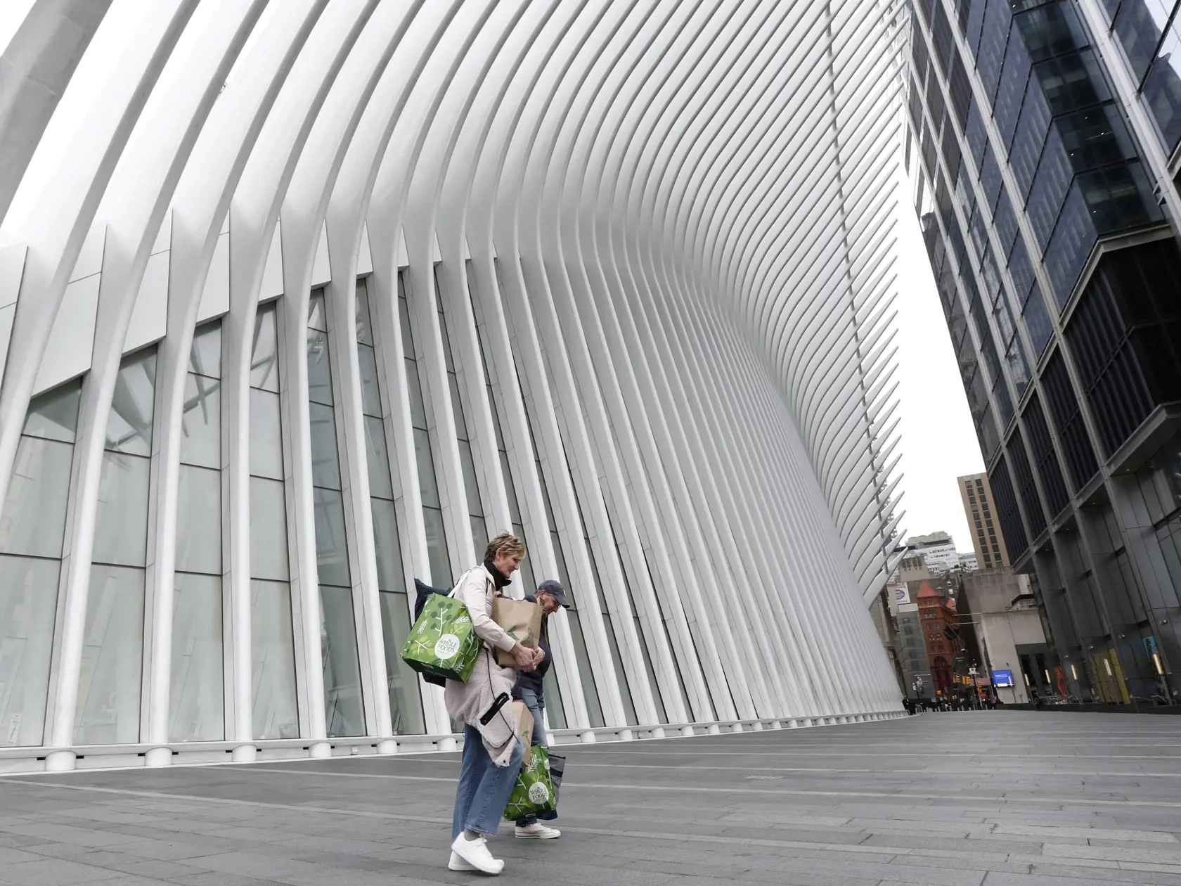 JB 18 New York - Dvaja ľudia si nesú nákup pri prechádzaní okolo Oculusu pri budove Svetového obchodného centra v New Yorku 5. apríla 2020. Americký prezident Donald Trump, ktorého administratíva čelí rovnako ako úrady vo viacerých štátoch kritike, že na šírenie nákazy dostatočne rýchlo nezareagovali, sa na nedeľňajšom večernom brífingu v Bielom dome vyjadril k situácii optimistickejšie než predtým viacerí predstavitelia zdravotníctva. "Začíname vidieť svetlo na konci tunela," vyhlásil Trump. Sp