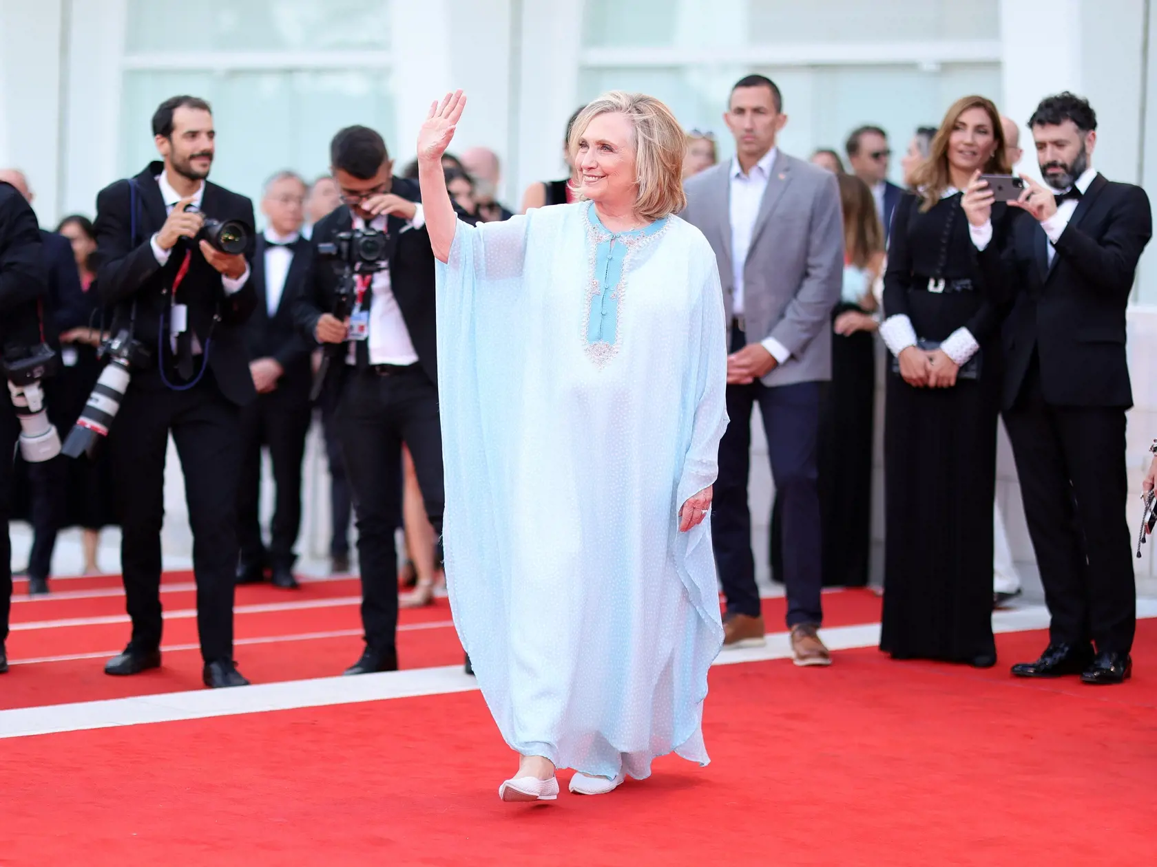 Luxusné róby, odhalené prsia aj extravagantné výstrelky zatienila na červenom koberci v Benátkach bývalá prvá dáma USA a ministerka zahraničných vecí Hillary Clintonová (74), ktorá sa nečakane objavila na premiére filmu White Noise Wednesday. Politička si vybrala oblečenie, ktoré sa hodilo k atmosfére neskorého leta. Vo vzdušnom modrom kaftane a v páre pohodlných topánok, ktoré pripomínali papuče, pôsobila na červenom koberci ako mecenáška.