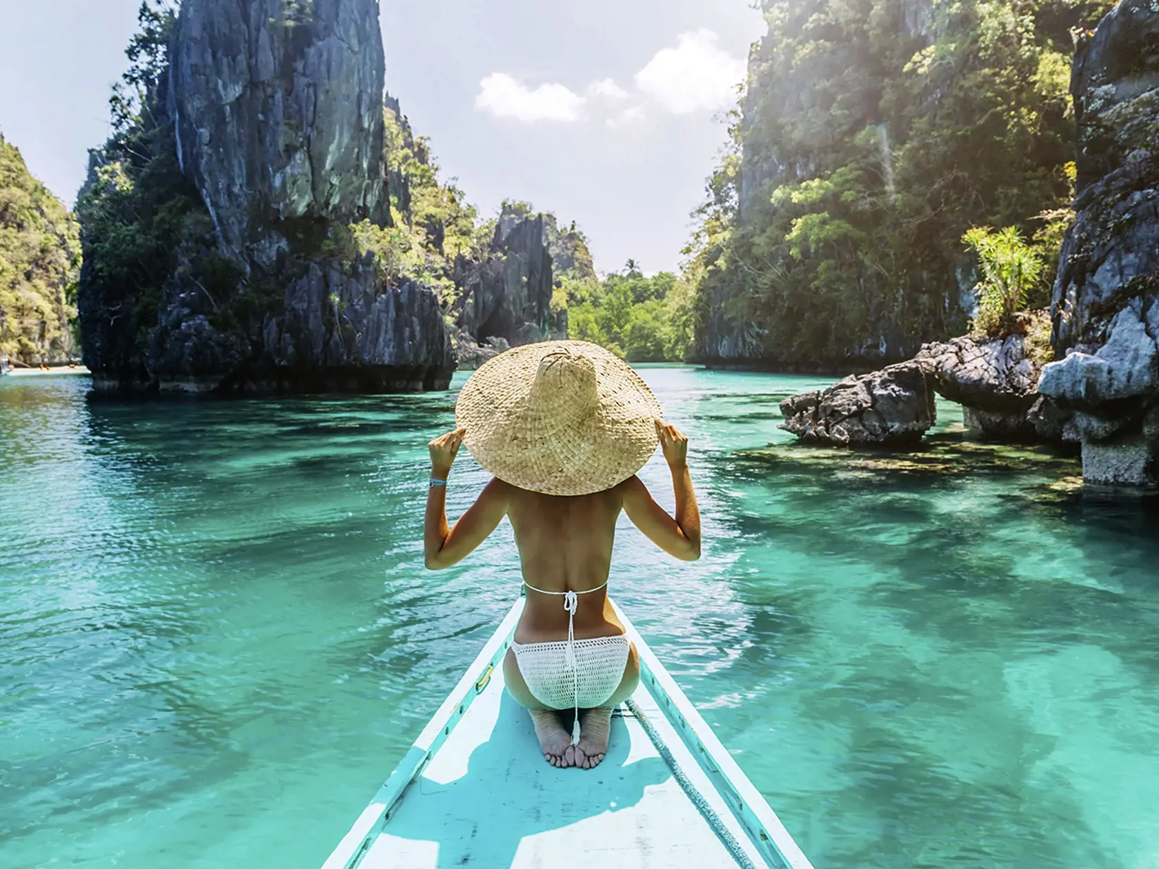 Back view of the young woman in straw hat relaxing on the boat and looking forward into lagoon. Travelling tour in Asia: El Nido, Palawan, Philippines.