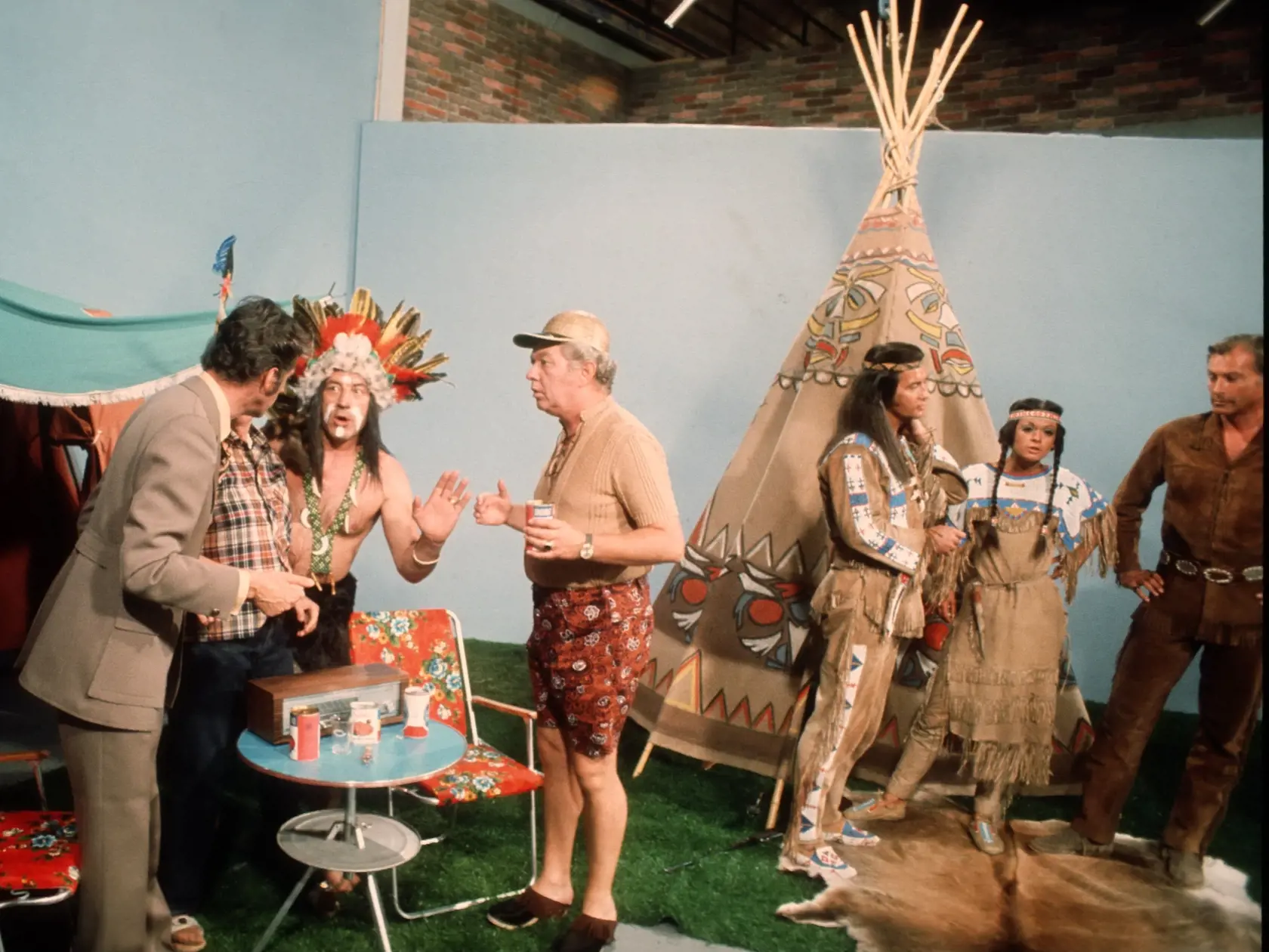 Rudi Carrell (li.), Lex Barker (als "Old Shatterhand"), Marie Versini, Pierre Brice (als "Winnetou") (v.r.n.l.), Kandidaten, ARD-Show "Rudi Carrell-Show", 20. Folge: "Schule", Deutschland, Europa, Indianer-Zelt, Kostüm, Feder, Federschmuck, Kopfschmuck, Campingausrüstung, Stuhl, Sänger, Entertainer, Schauspieler, Schauspielerin, 05.06.1971; (Photo by Peter Bischoff/Getty Images)