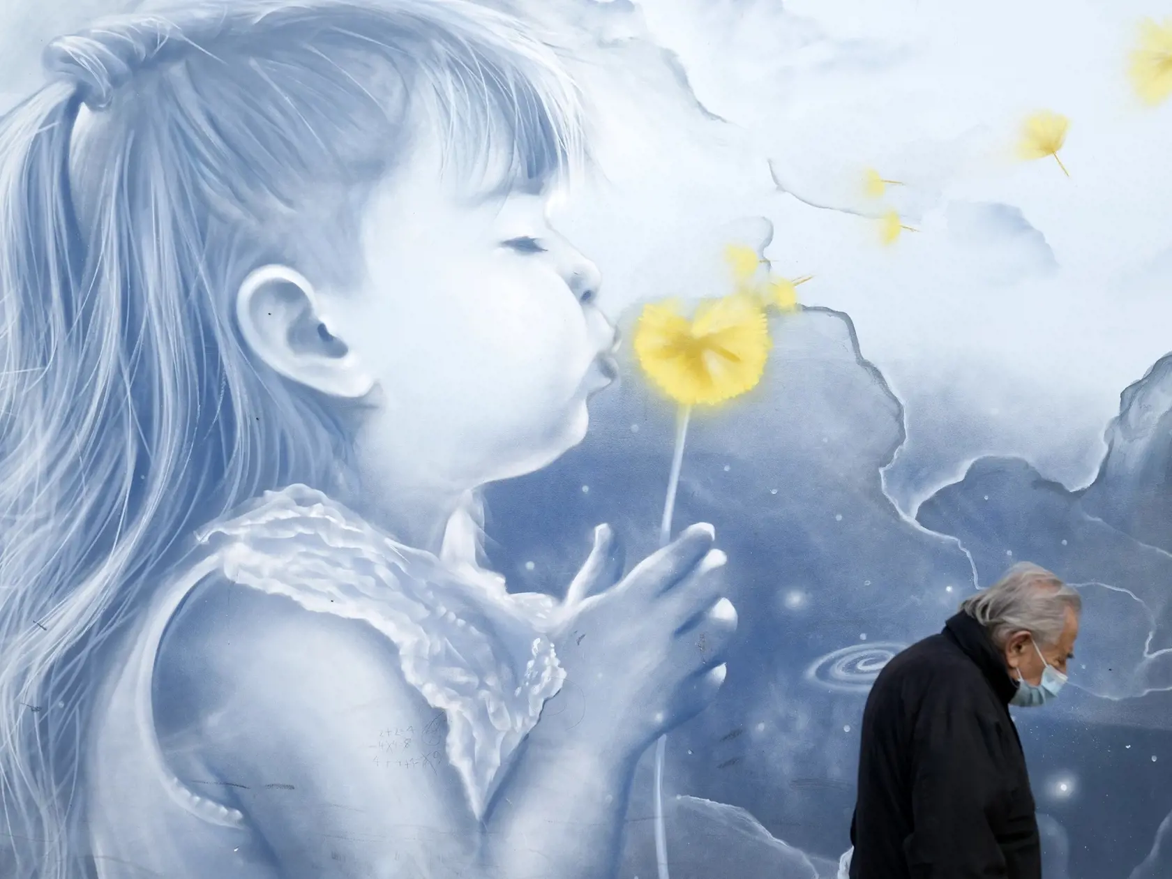 Muž s ochranným rúškom proti šíreniu ochorenia COVID-19 kráča pred grafitom na stanici metra.