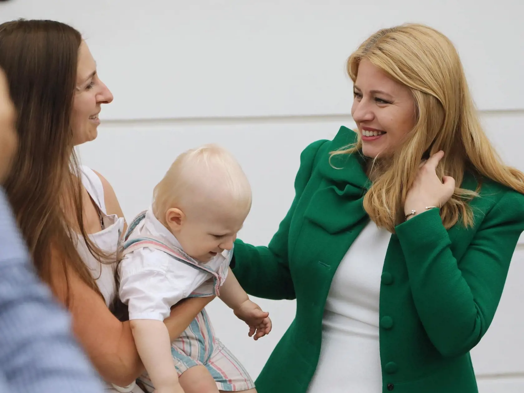 Usmiata prezidentka upiera síce pohľad na matku, ale pravicou drží za plece malého nespokojenca, ktorý ba asi radšej ako na rukách chcel "pochodovať" po svojich.