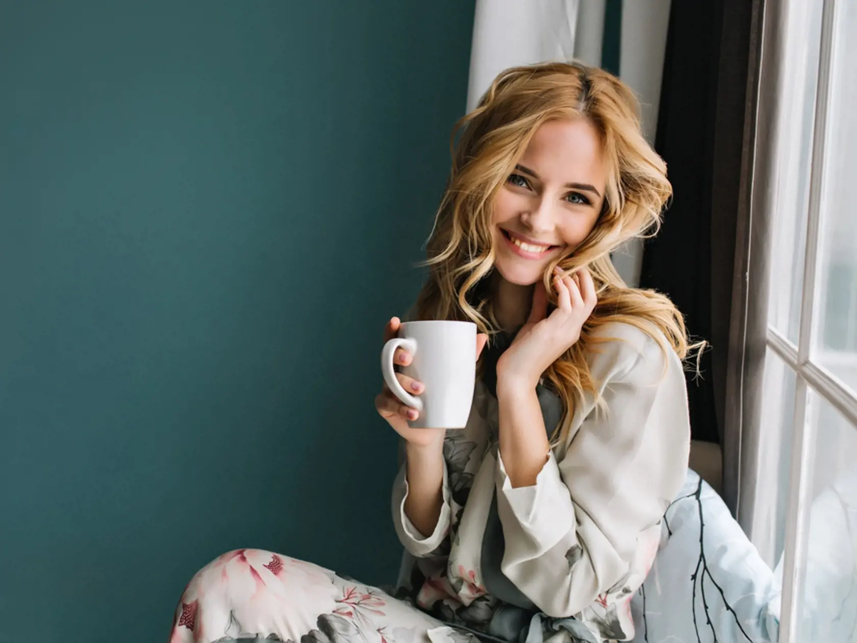 Cheerful,Blonde,Woman,Relaxing,And,Sitting,On,Window,Sill,,Holding