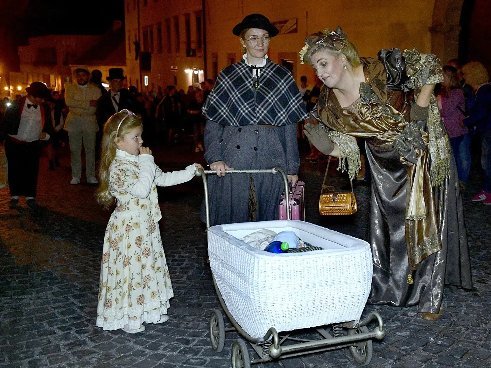 Milostivú pani vpravo zaujalo bábätko v kočiariku ženy, ktorá je vychystaná na cestu. Svedčí o tom kufrík a cestovný plášť.