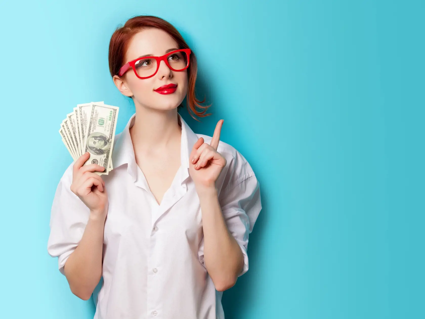 Portrait of redhead women in red glasses with money on blue background