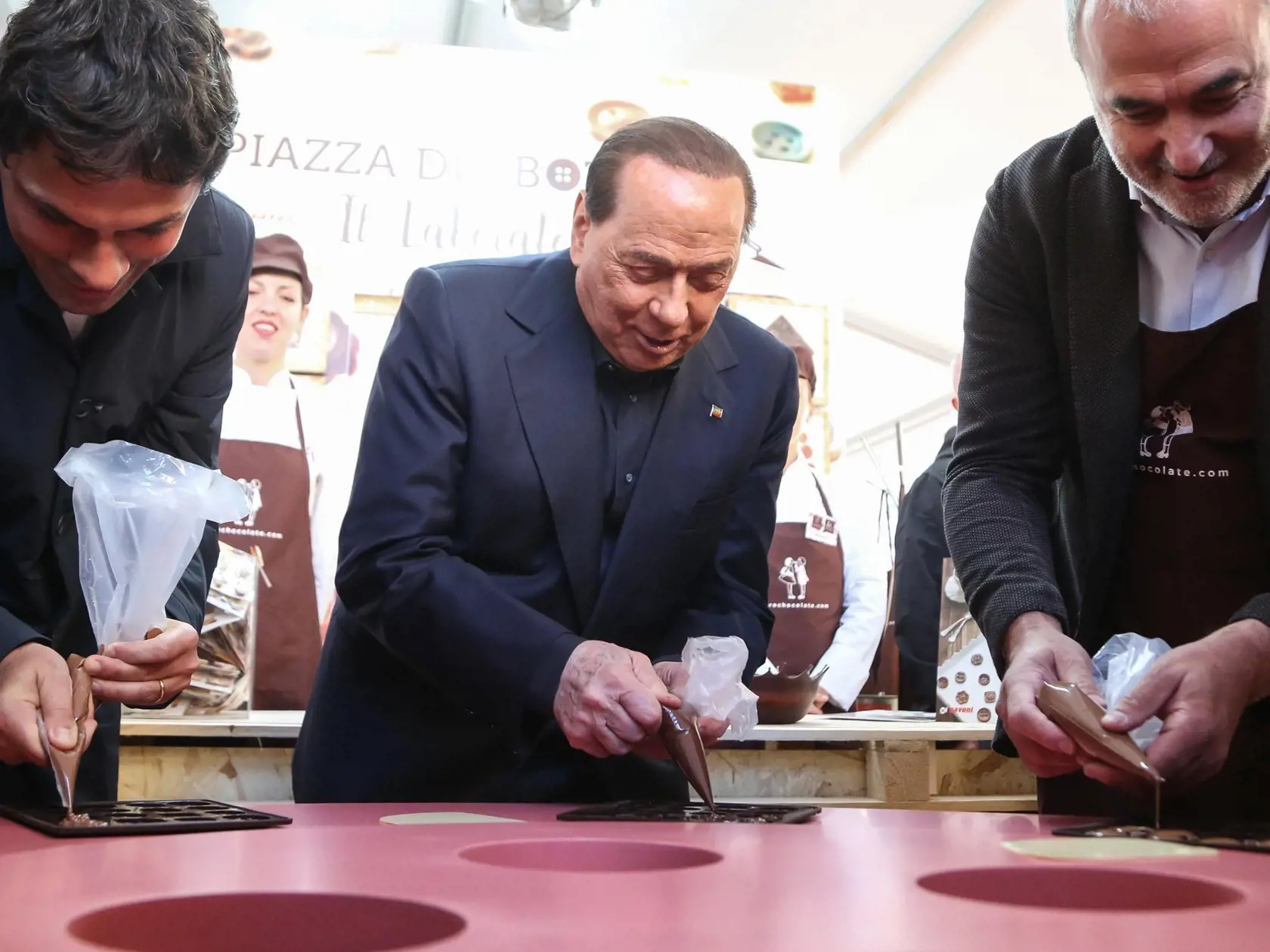 Líder strany Forza Italia a taliansky expremiér Silvio Berlusconi (uprostred), starosta mesta Perugia Andrea Romizi (vľavo) a patrón Eurochocolate Eugenio Guarducci plnia formičky čokoládou počas podujatia Eurochocolate v talianskom meste Perugia v piatok 18. októbra 2019.