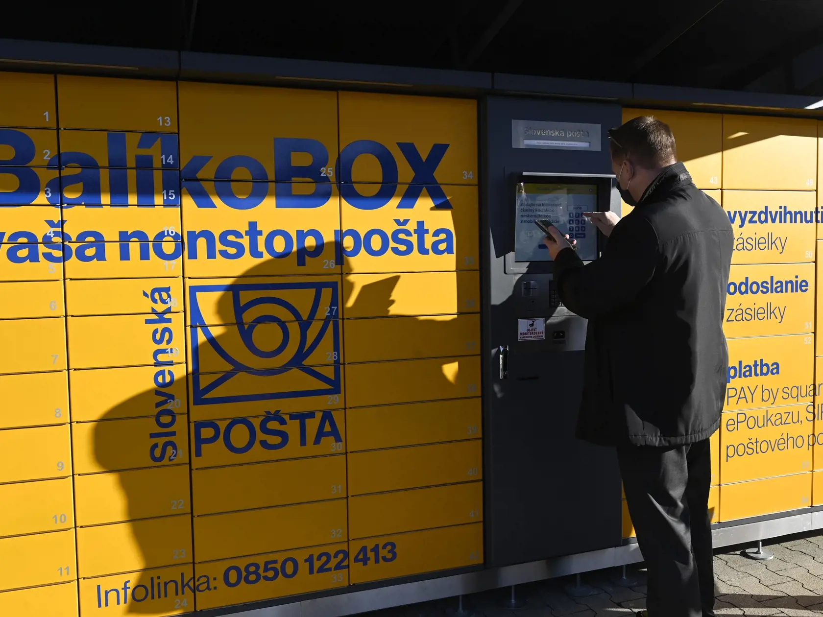 Slovenská pošta spustila prevádzku prvého balíkovoboxu v meste Púchov, 1. februára 2021. Cez balíkoboxy môžu zákazníci okrem vyzdvihovania a podaja balíkov v predplatených obaloch realizovať už aj platobné transakcie, úhradu poštových poukazov, ePoukazy, SIPO či faktúry s PAY by Square kódom.  Na snímke predseda predstavenstva Slovenskej pošty Martin Ľupták predvádza, ako si zákazník vyzdvihne balík z balíkoboxu. FOTO TASR - Radovan Stoklasa