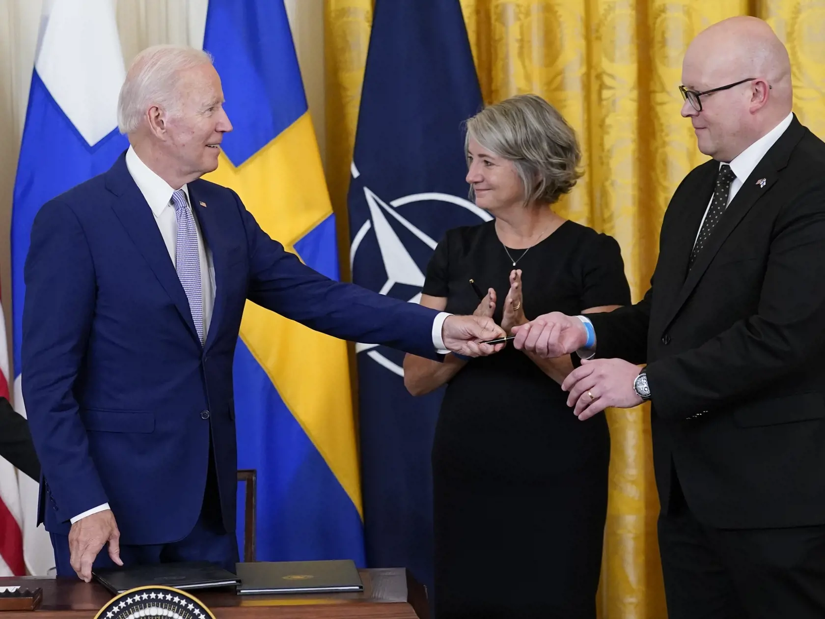Americký prezident Joe Biden (vľavo) podáva pero fínskemu veľvyslancovi v USA Mikkovi Hautalpvo po podpise dokumentu povoľujúceho vstup Fínska a Švédska do NATO, uprostred švédska veľvyslankyňa v USA Karin Olofsdotterová 9. augusta 2022 vo Washingtone.