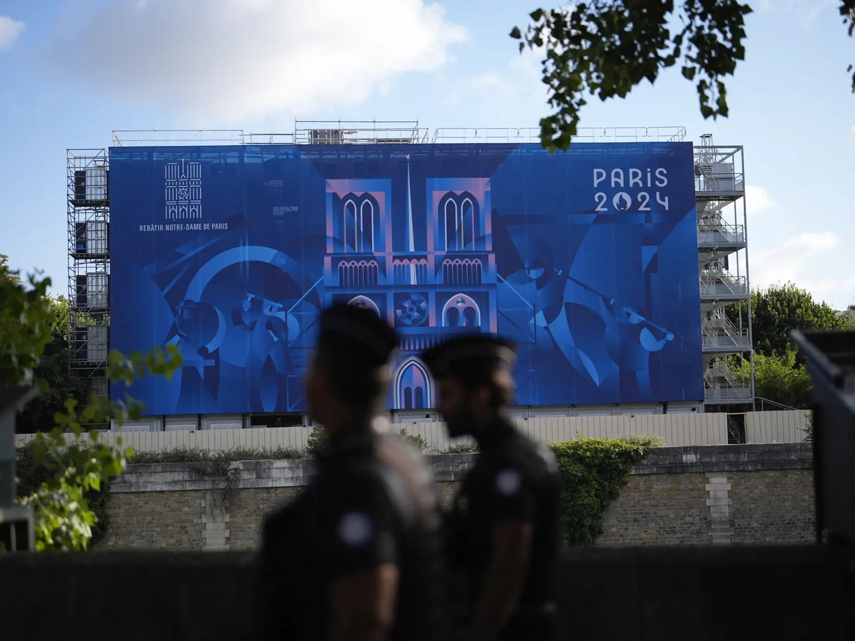 Policajti kráčajú okolo rieky Seina a obrovského transparentu s nápisom Olympijské hry 2024 v Paríži vo francúzskej metropole v pondelok 22. júla 2024. Letné olympijské hry v Paríži sa začnú v piatok 26. júla a potrvajú do 11. augusta.