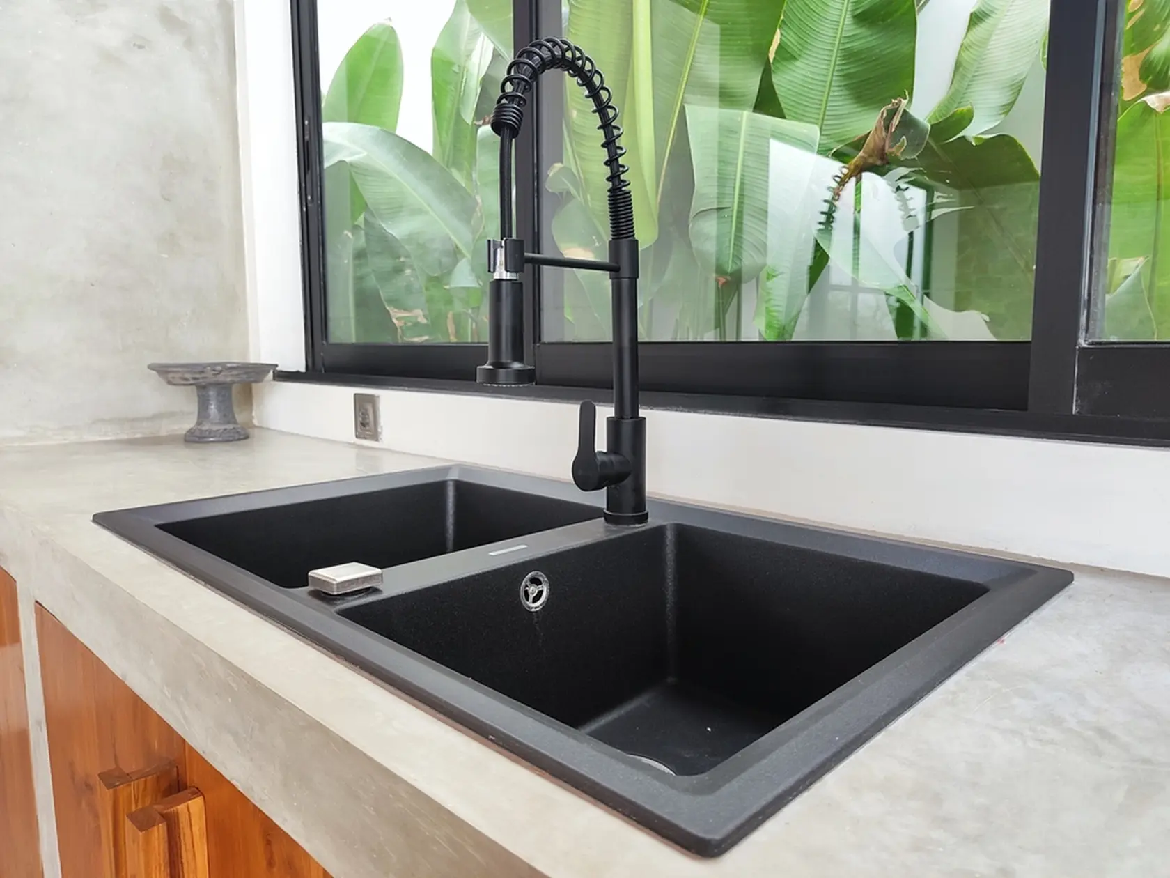A modular black kitchen sink made of quartz granite with double bowls, top-mounted on a polished cement countertop in the kitchen area of a tropical villa