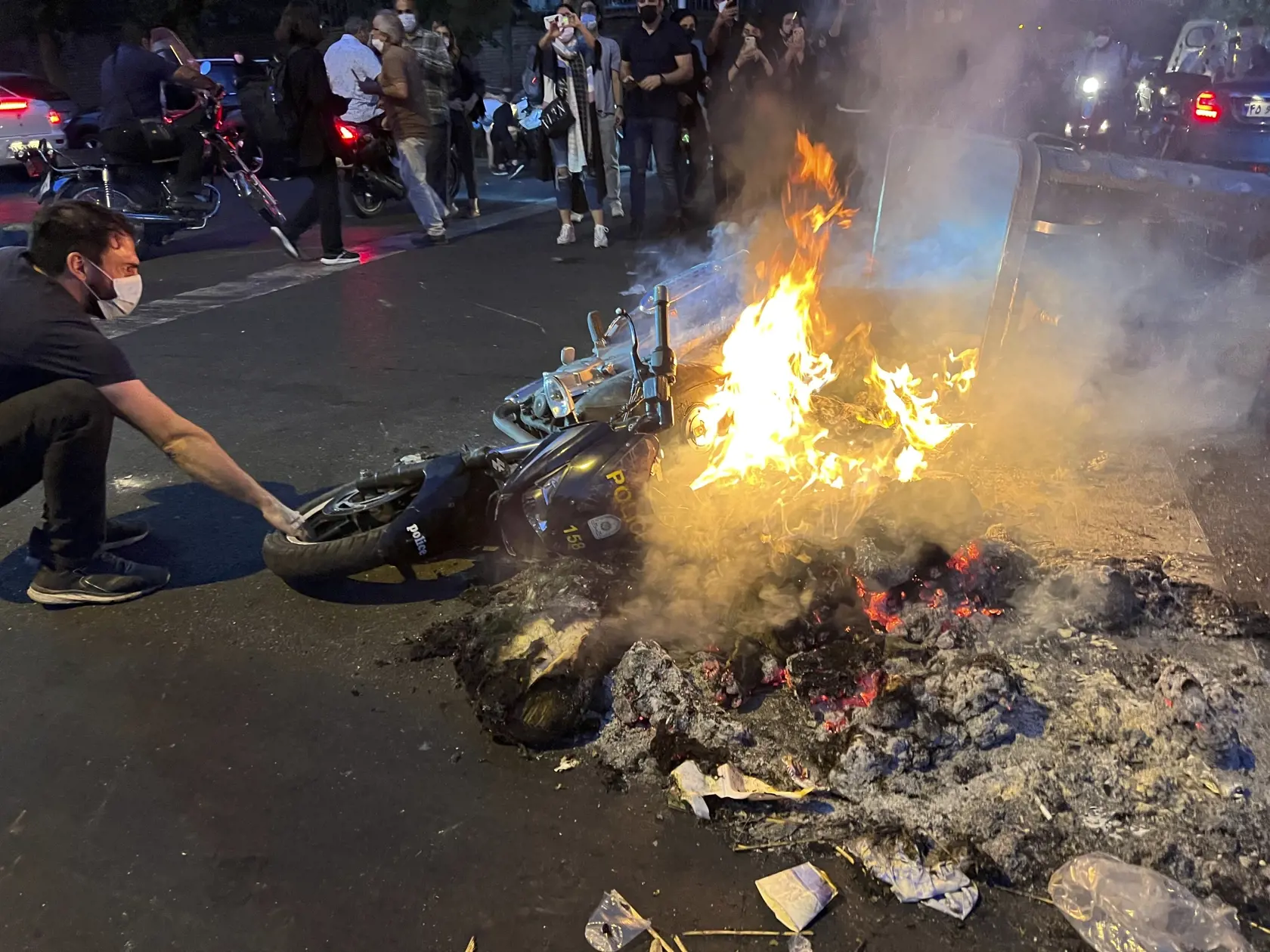 Na snímke z pondelka 19. septembra 2022 od osoby, ktorá nie je zamestnaná v agentúre Associated Press (AP), a ktorú získala agentúra AP mimo Iránu, muž vyťahuje horiaci policajný motocykel počas protestu proti smrti mladej iránskej ženy Mahsá Amíníovej v centre Teheránu.