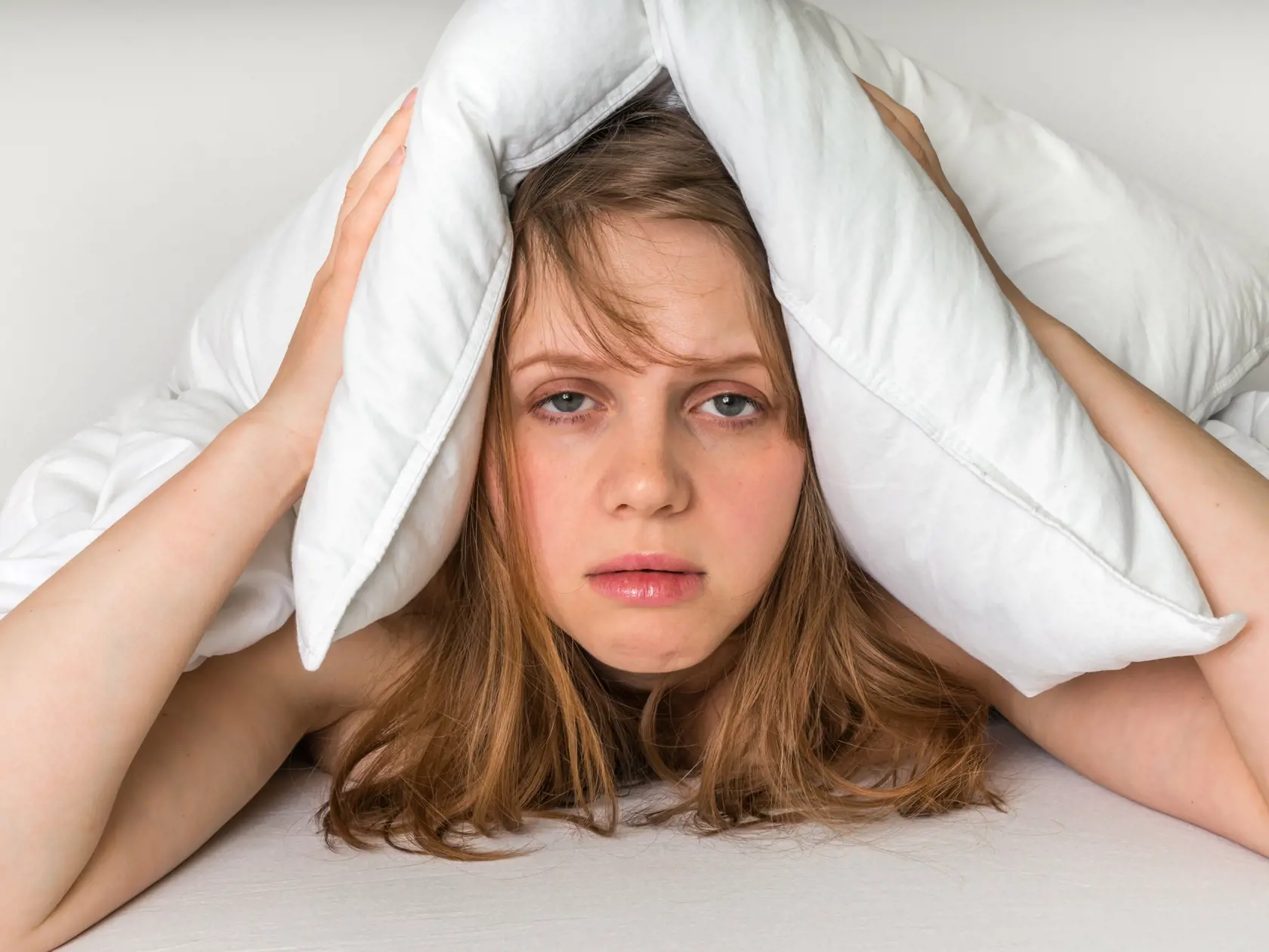 Young,Woman,In,Bed,Covering,Ears,With,Pillow,Because,Of
