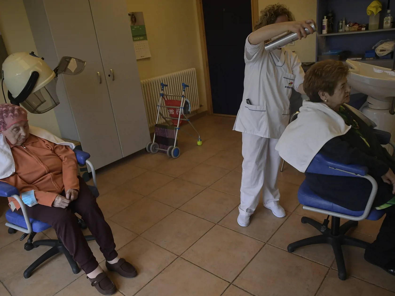 WA 38 Erno - Deväťdesiatročná Maribel Elizondová s natáčkami vo vlasoch sedí pri sušiči a kaderníčka Gloria Cerdanová lakuje vlasy 84-ročne Luise Tollarovej v kaderníckom salóne, ktorý sa nachádza v domove seniorov v obci Erro, zhruba 30 km od Pamplony na severe Španielska v pondelok 22. marca 2021. Raz do týždňa, každý pondelok, prichádza kaderníčka Gloria Cerdanová ponúknuť svoje služby do domova seniorov v tejto malej obci. FOTO TASR/AP   

90 Maribel Elizondo, left, sits as 84 year old Luisa