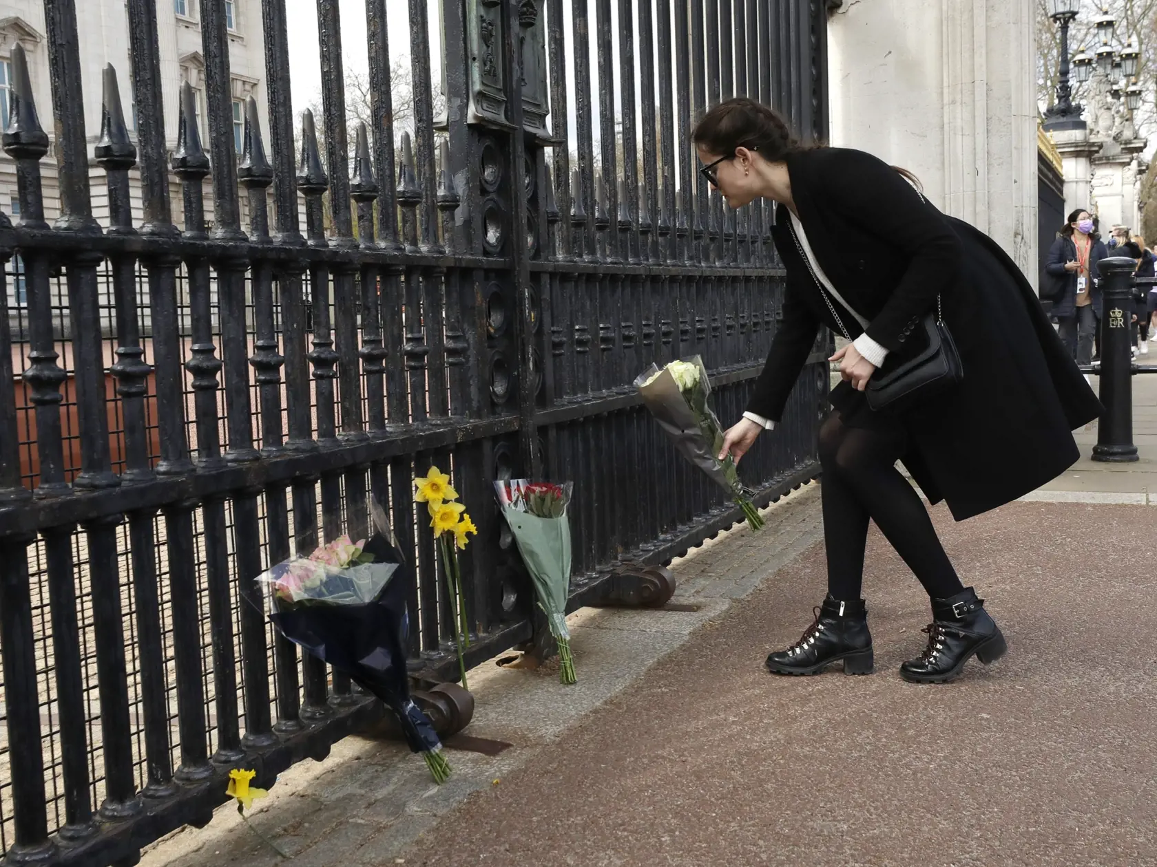 KK5 Londýn - Žena kladie kvety pred bránu Buckinghamského paláca po prečítaní oznámenia o úmrtí britského princa Philipa 9. apríla 2021 v Londýne. Britský princ Philip, manžel kráľovnej Alžbety II., zomrel v piatok vo veku 99 rokov. Oznámil to Buckinghamský palác.  "Jeho kráľovská výsosť zomrela dnes ráno pokojne na Windsorskom zámku," dodal palác s tým, že ďalšie informácie zverejnia v náležitom čase. FOTO TASR/AP
A woman lays flowers in front of the gate of Buckingham Palace in London after an
