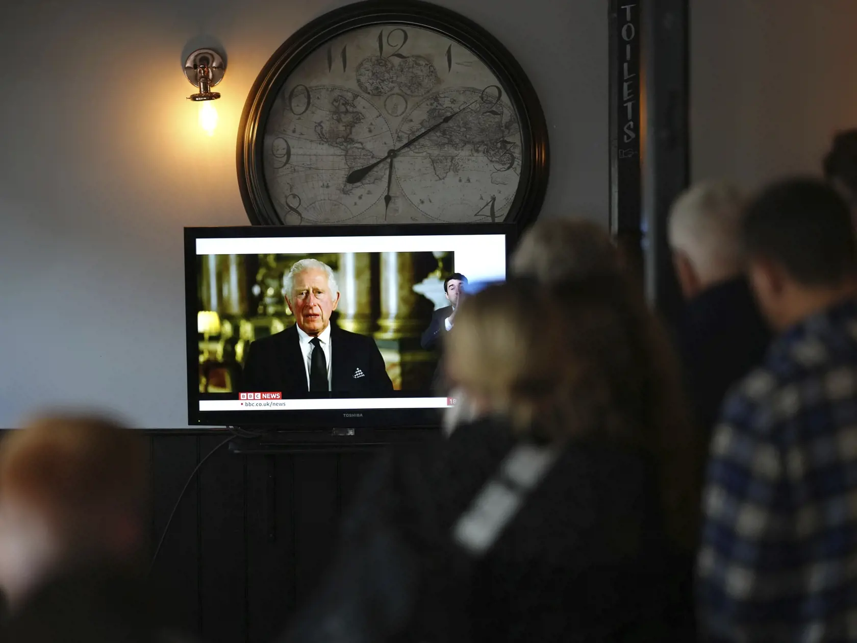 Na snímke ľudia sledujú prvý príhovor nového britského kráľa Karola III. ako monarchu cez televízny prenos po smrti britskej kráľovnej Alžbety II. v Londýne 9. septembra 2022. Karol III. sa v piatok podvečer prvýkrát prihovoril verejnosti prostredníctvom videopríhovoru. Zosnulú Alžbetu II. v ňom označil za inšpiráciu pre neho samého aj celú kráľovskú rodinu a prisľúbil, že bude pokračovať v jej celoživotnej službe. FOTO TASR/AP