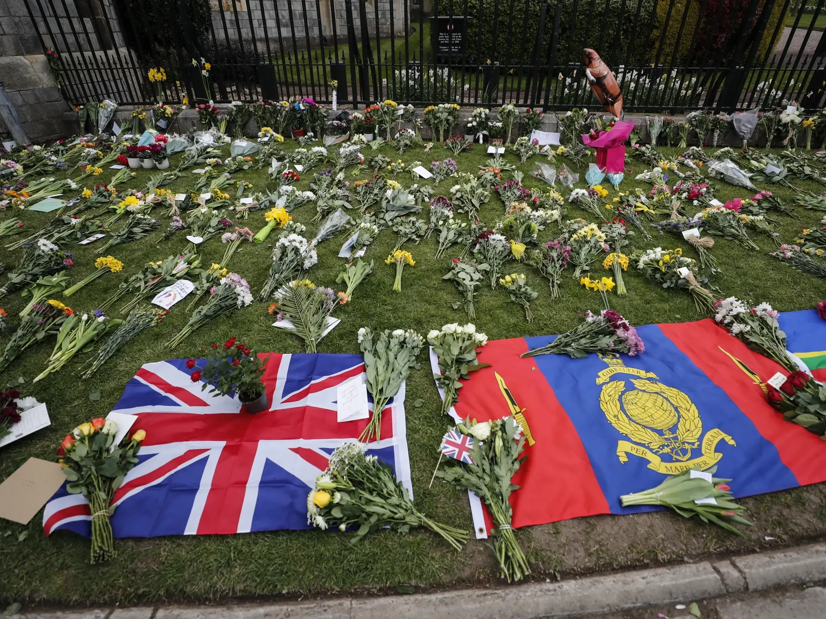 KK61 Windsor - Vlajky ležia medzi kvetmi pred Windsorským hradom 9. apríla 2021. Britský princ Philip, manžel kráľovnej Alžbety II., zomrel v piatok vo veku 99 rokov. Oznámil to Buckinghamský palác.  "Jeho kráľovská výsosť zomrela dnes ráno pokojne na Windsorskom zámku," dodal palác. FOTO TASR/AP
Flags lay amongst flowers outside of Windsor Castle in Windsor, England after the announcement regarding the death of Britain's Prince Philip, Friday, April 9, 2021. Buckingham Palace officials say Prin