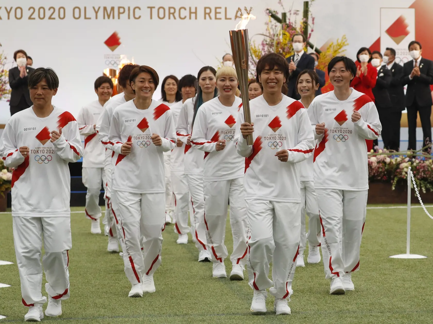 WA 5 Naraha - Japonská futbalová reprezentantka Azusa Iwašimizuová nesie olympijskú pochodeň v spoločnosti svojich spoluhráčok počas štartu štafety s olympijskou pochodňou hier v Tokiu po krajine v J-Village vo Fukušime vo štvrtok 25. marca 2021. Štafeta sa začala v J-Village, čo je futbalový tréningový komplex neďaleko jadrovej elektrárne Fukušima, kde sa pred 10 rokmi stala najhoršia jadrová havária v histórii Japonska, a potrvá 121 dní. Pri štafete s olympijským ohňom sa vystrieda okolo 10.00