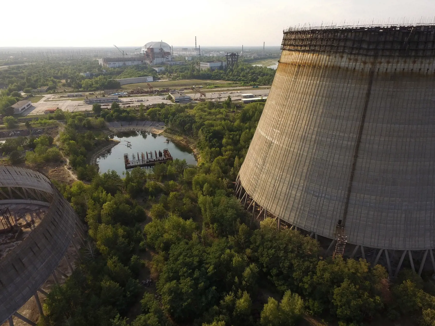 CHORNOBYL', UKRAINE - AUGUST 19:  In this aerial view two partially-constructed and abandoned cooling towers stand as the new enclosure built over stricken reactor number four is seen in the distance behind at the Chernobyl nuclear power plant on August 19, 2017 near Chornobyl', Ukraine. On April 26, 1986 reactor number four exploded after a safety test went wrong, spreading radiation over thousands of square kilometers in different directions. Ukraine and Belarus are still challenged by the con