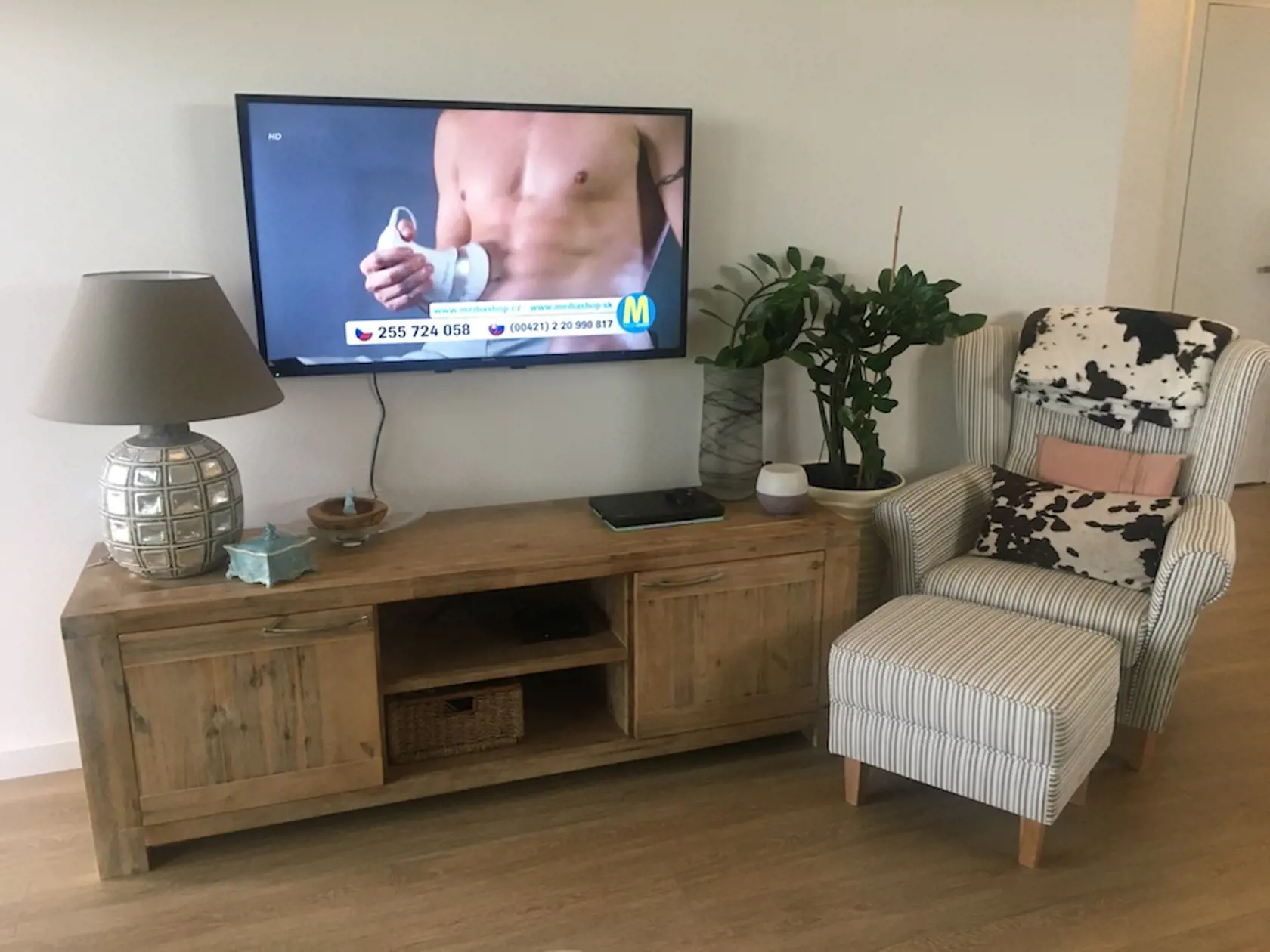 Oproti sedacej súprave je komoda z masívneho dreva, nad ňou visí zo steny televízor a nechýba ani kreslo s taburetkou na oddych s knihou v ruke a výhľadom na terasu.