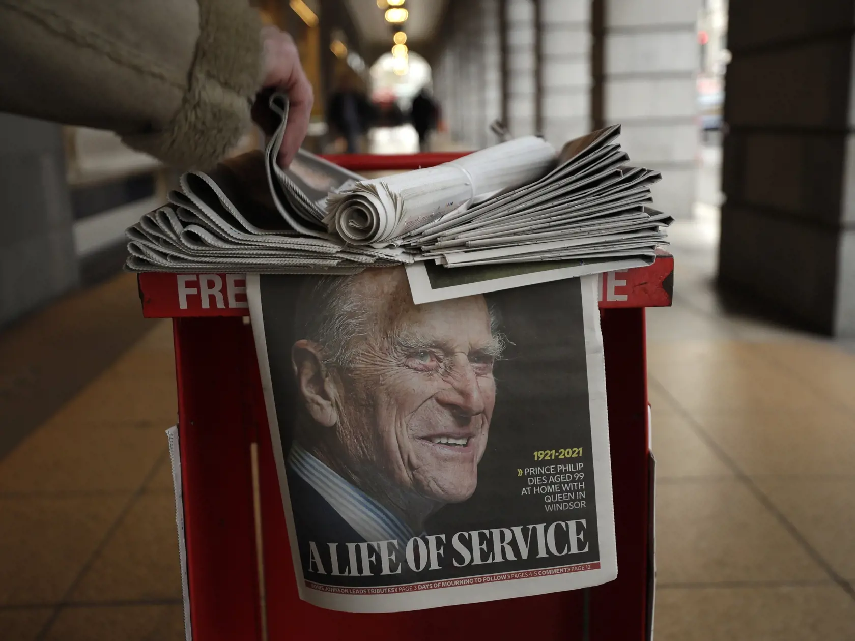 KK63 Londýn - Na snímke noviny s fotografiou zosnulého britského princa Philipa na titulke v Londýne 9. apríla 2021. Britský princ Philip, manžel kráľovnej Alžbety II., zomrel v piatok vo veku 99 rokov. Oznámil to Buckinghamský palác.  "Jeho kráľovská výsosť zomrela dnes ráno pokojne na Windsorskom zámku," dodal palác s tým, že ďalšie informácie zverejnia v náležitom čase. FOTO TASR/AP
A person takes a copy of a newspaper with a tribute to Britain's Prince Philip on the front page at Leicester S