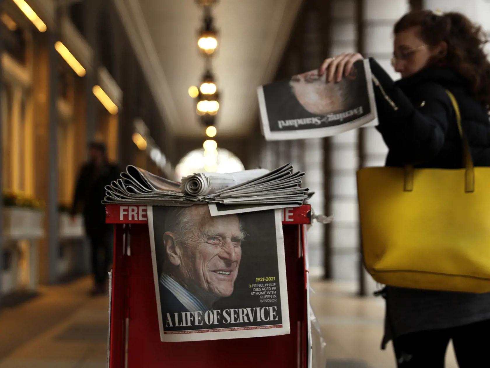 WA 34 Londýn - Žena si berie noviny v Londýne, ktoré majú na titulnej stránke fotografiu britského princa Philipa, ktorý zomrel vo veku 99 rokov v piatok 9. apríla 2021. Manžel kráľovnej Alžbety II. zomrel v piatok ráno vo veku 99 rokov - dva mesiace pred svojimi 100. narodeninami - na Windsorskom zámku. Britská vláda i kráľovská rodina vyzvali ľudí, aby naďalej dodržiavali pandemické nariadenia a nezúčastňovali sa na spomienkových zhromaždeniach. Pred Buckinghamský palác medzitým položilo kvety