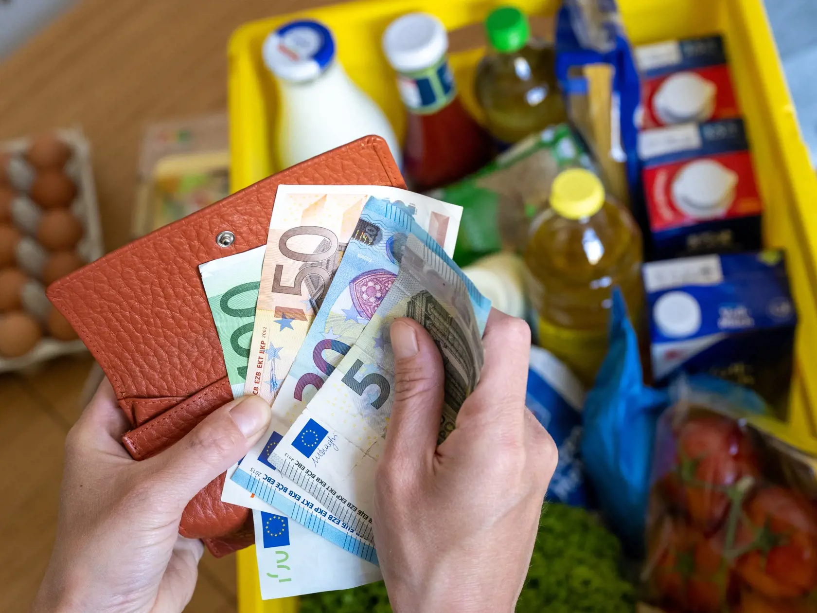 Žena drží v rukách eurové bankovky nad nákupom.