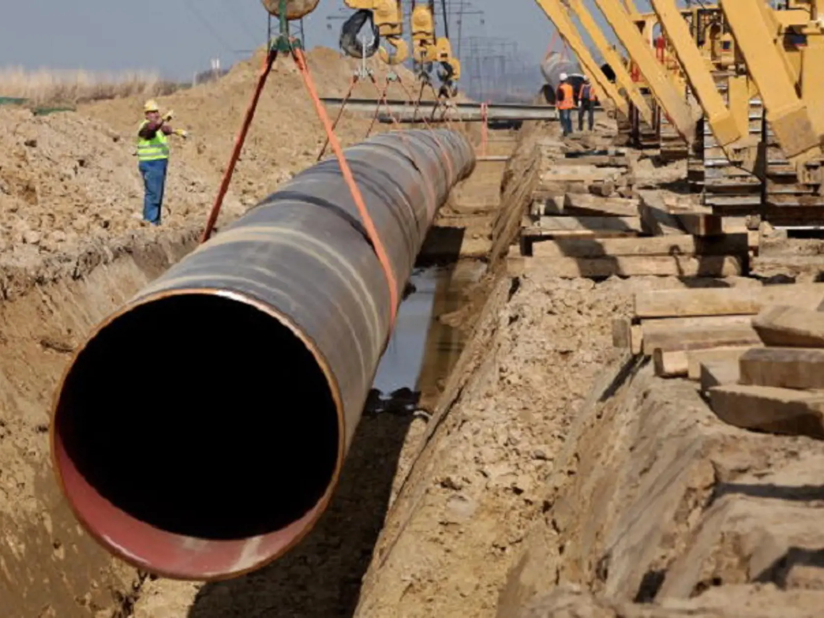 LUBMIN, GERMANY - APRIL 08:  A worker shouts commands as cranes lower a section of pipe into the ground for the OPAL pipeline on April 8, 2010 near Lubmin, Germany. The OPAL and NEL pipelines will carry natural gas from Russia arriving through the Nord Stream pipeline from the Baltic Sea across Germany and to other countries in Europe. The Nord Stream project delivers Russian natural gas directly to western Europe and avoids countries in between, such as Poland and Ukraine.  (Photo by Sean Gallu