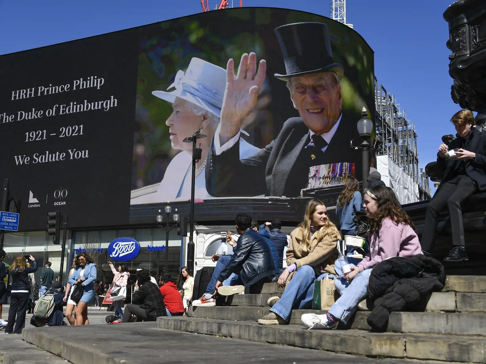 JB 58 Londýn - Ľudia sedia neďaleko portrétu britského princa Philipa, manžela britskej kráľovnej Alžbety II., ktorý zomrel minulý piatok vo veku 99 rokov, zobrazenom na gigantickej obrazovke Piccadilly Circus v Londýne 17. apríla 2021 pred jeho dnešným pohrebom v areáli Windsorského zámku vo Windsore. Pohreb sa uskutoční v sobotu popoludní v areáli Windsorského zámku, informovala v pondelok stanica BBC. Pohrebné obrady sa budú konať v tamojšej kaplnke svätého Juraja o 15.00 h miestneho času (16