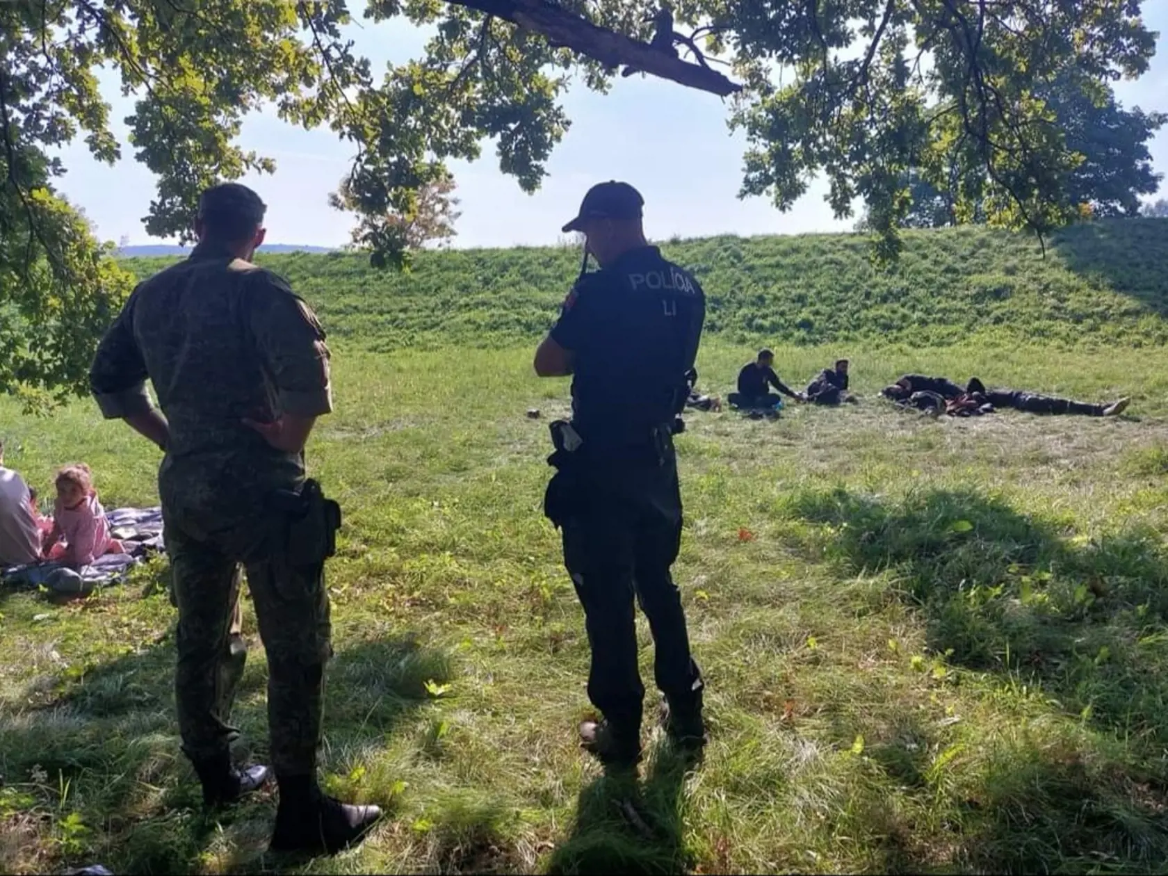 Policajti sa boli pozrieť aj na migrantov posedávajúcich na tráve pri hrádzi.
