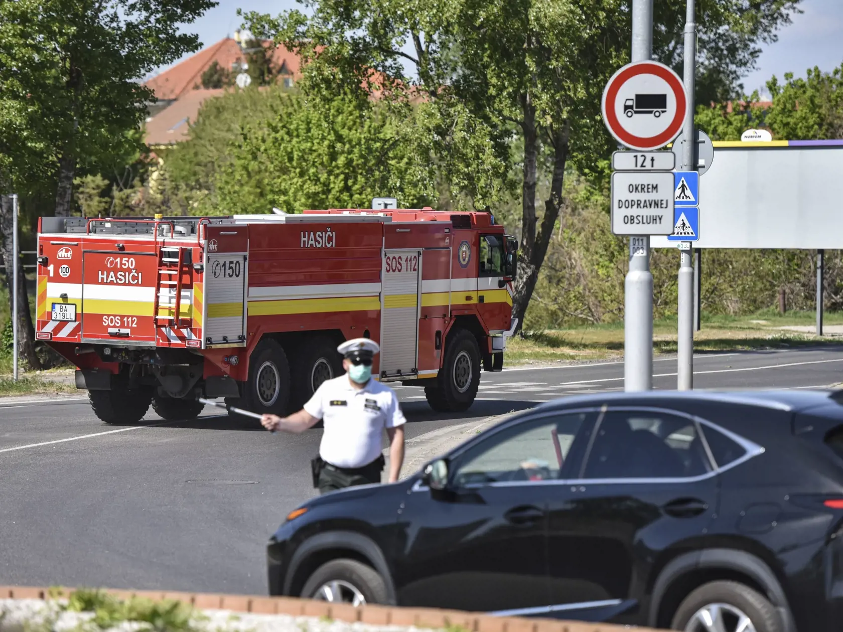 Na snímke príslušník Policajného zboru SR odkláňa dopravu na kruhovom objazde v dôsledku požiaru na Ráztočnej ulici vo Vrakuni, v pozadí príslušníci Hasičského záchranného zboru SR smerujú na miesto požiaru 25. apríla 2020 v Bratislave. FOTO TASR - Pavol Zachar