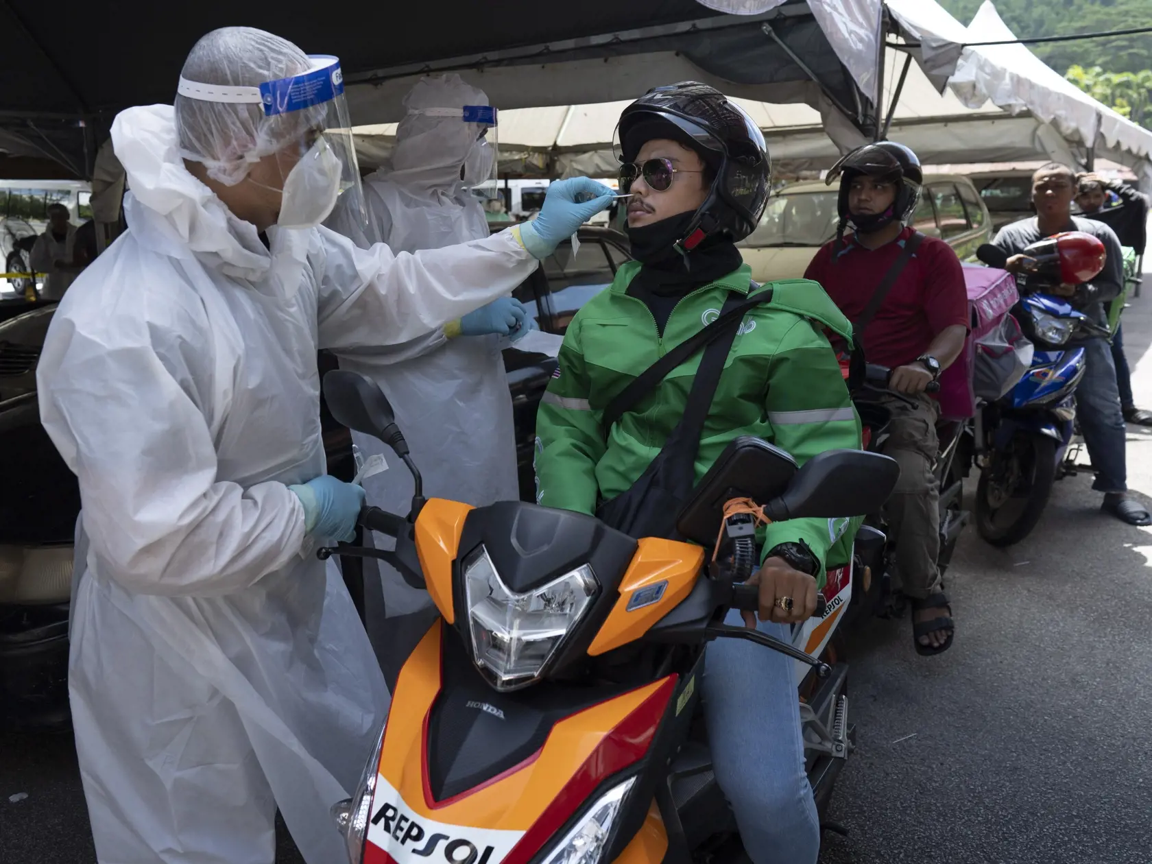 Zdravotníci odoberajú vzorky roznášačom jedál na motocykloch počas mobilného testovania na COVID-19 na zabránenie šíreniu nového koronavírusu v Gombaku pri Kuala Lumpure.