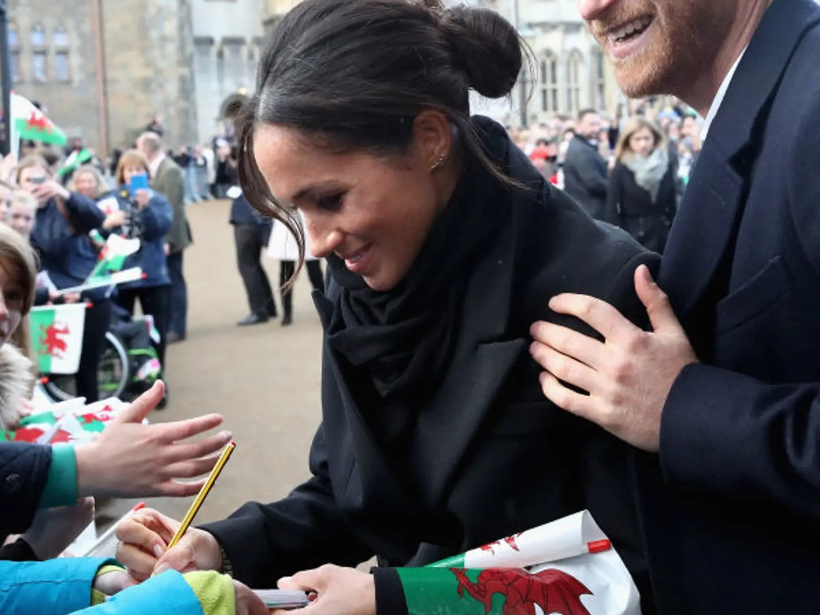 CARDIFF, WALES - JANUARY 18:  Meghan Markle writes a note for 10 year old Caitlin Clarke from Marlborough Primary School as Prince Harry looks on during a walkabout at Cardiff Castle on January 18, 2018 in Cardiff, Wales.  (Photo by Chris Jackson/Getty Images)