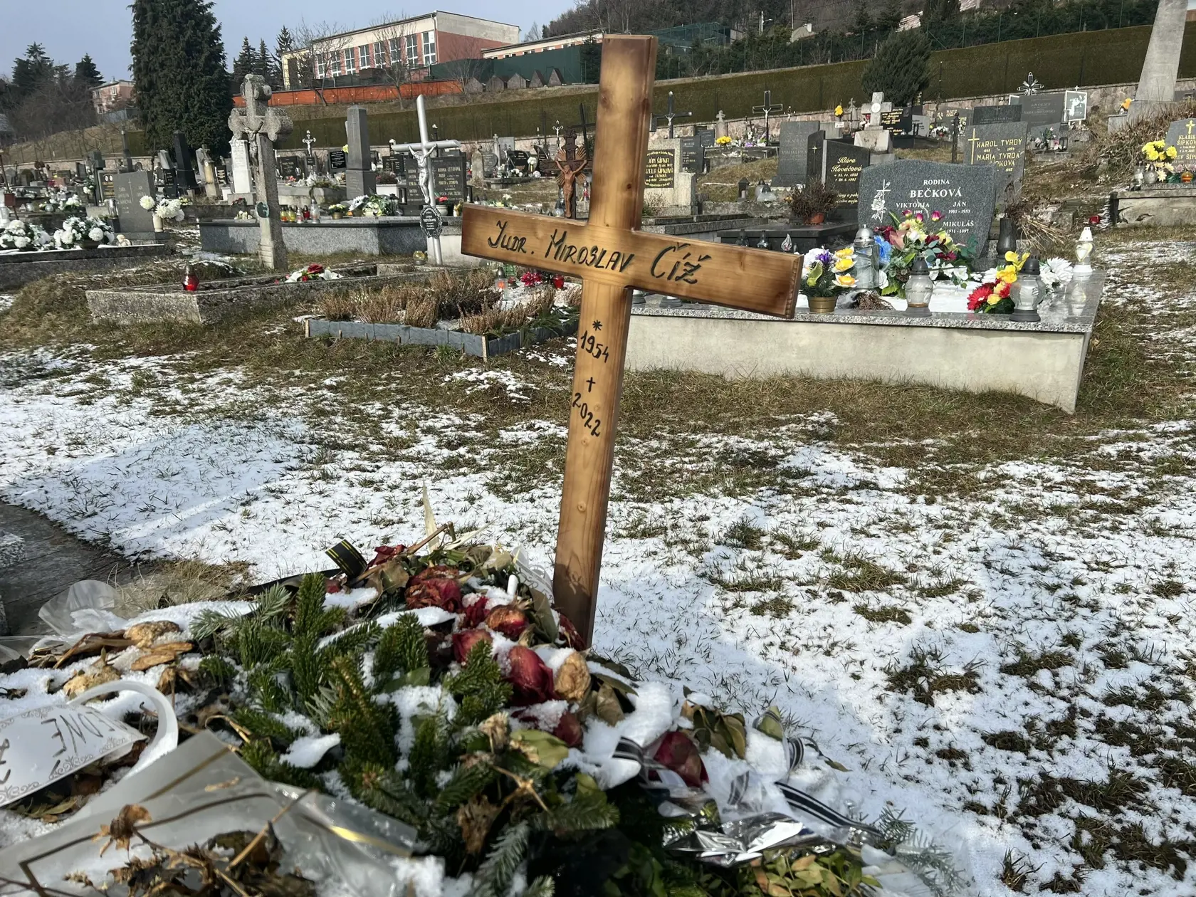 Namiesto pomníka tu dočasne stojí len jednoduchý drevený kríž a hrob pôsobí ako keby sa oň nik nestaral - ležia na ňom staré kvety ešte od pohrebu.