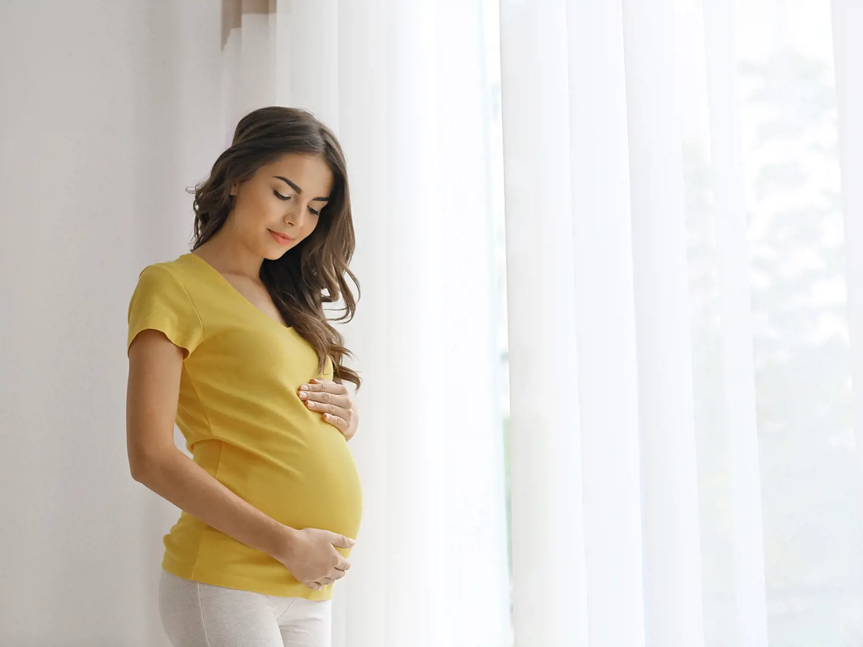 Young,Beautiful,Pregnant,Woman,Standing,Near,Window,At,Home