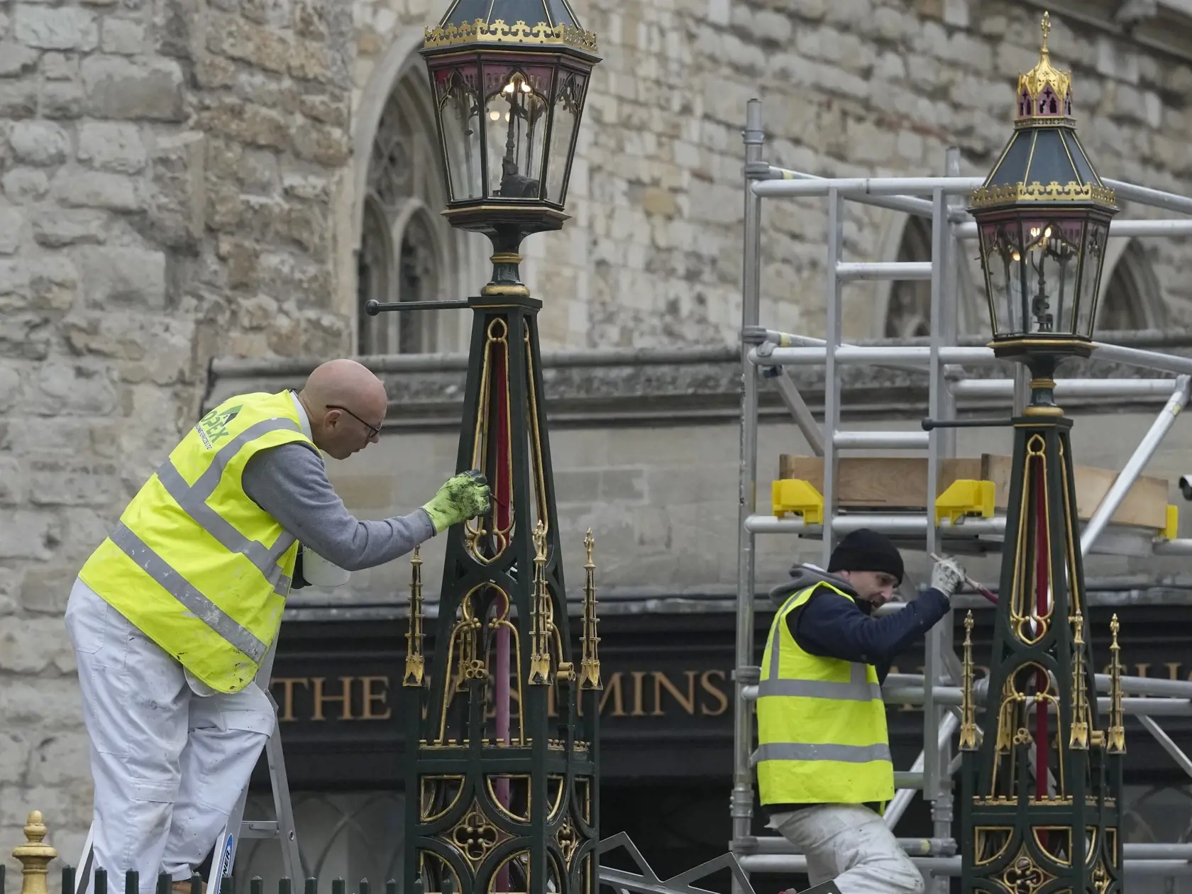 Maliari premaľovávajú lampy pred Westminsterským opátstvom počas príprav na korunováciu britského kráľa Charlesa III. v Londýne 27. apríla 2023.