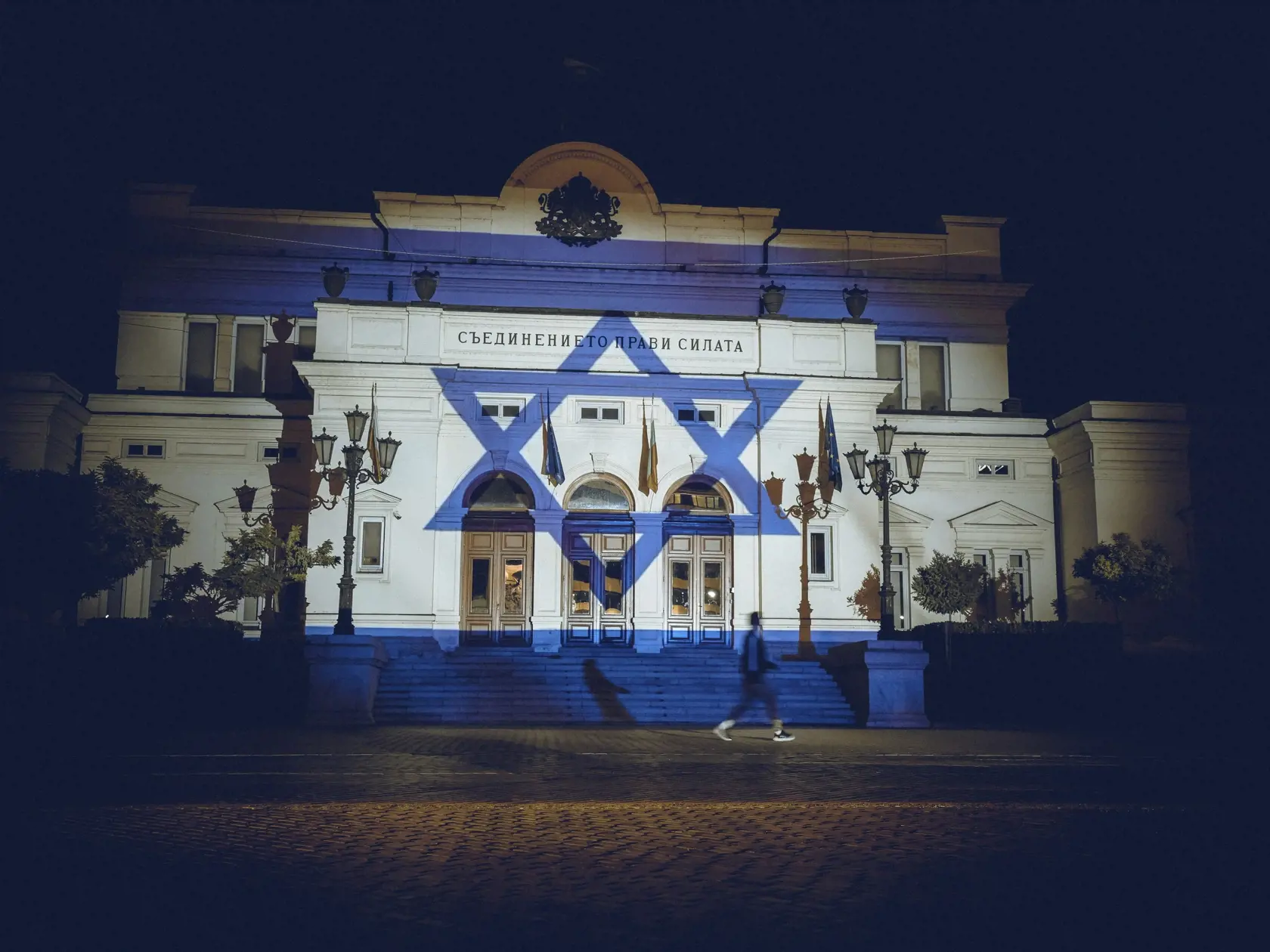 KK11 Sofia -  Izraelská vlajka je vysvietená na budove parlamentu na znak solidarity s Izraelom 8. októbra 2023 v Sofii. Od sobotného rána, keď Hamas podporovaný Iránom začal z pásma Gazy útočiť na Izrael, ktorý odpovedal protiútokmi, prišli na oboch stranách o život už stovky ľudí. FOTO TASR/AP

A person is passing in front of the flag of Israel, that is projected on the Bulgarian Parliament building, in Sofia, Bulgaria, Sunday, Oct. 8,2023, to show support for Israel following Hamas' unprecede