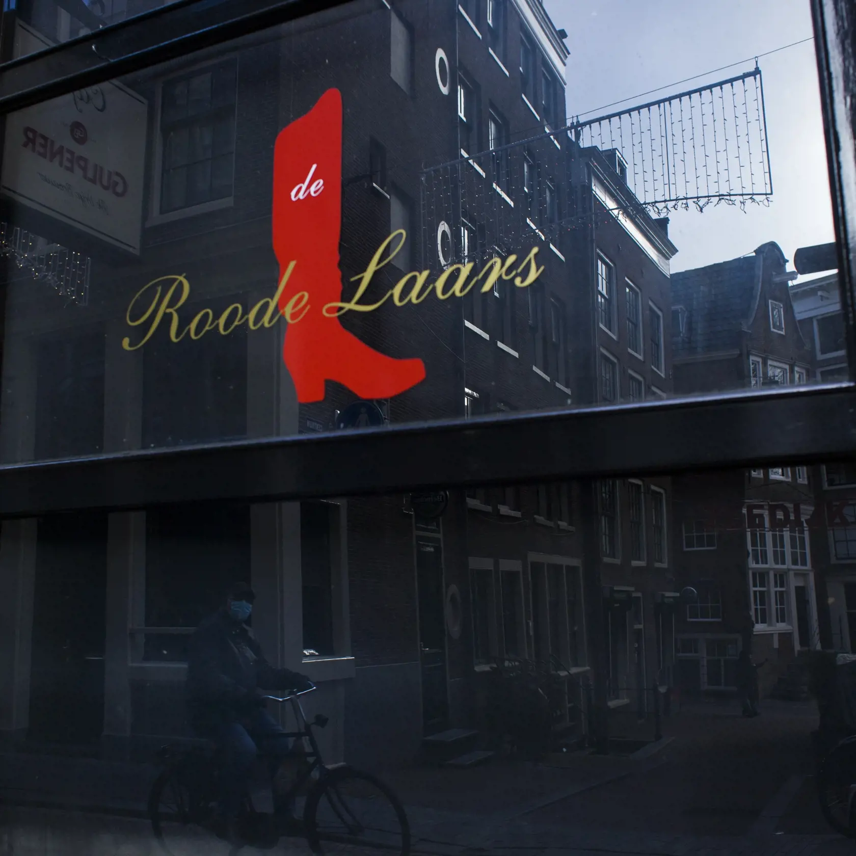 JB 23 Amsterdam - Cyklista s ochranným rúškom v odraze vo výklade kaviarne Red Boot počas lockdownu v štvrti Red Light District v Amsterdame 4. februára 2021. Holandsko predĺži platnosť mnohých opatrení proti nákaze koronavírusom až do 2. marca a dôvodom sú obavy z "rýchleho šírenia" variantu, prvýkrát zisteného v Británii. V utorok to oznámil holandský premiér Mark Rutte, ktorého citovala tlačová agentúra AFP. Rutte však potvrdil, že základné školy sa znovu otvoria 8. februára a na budúci týžde