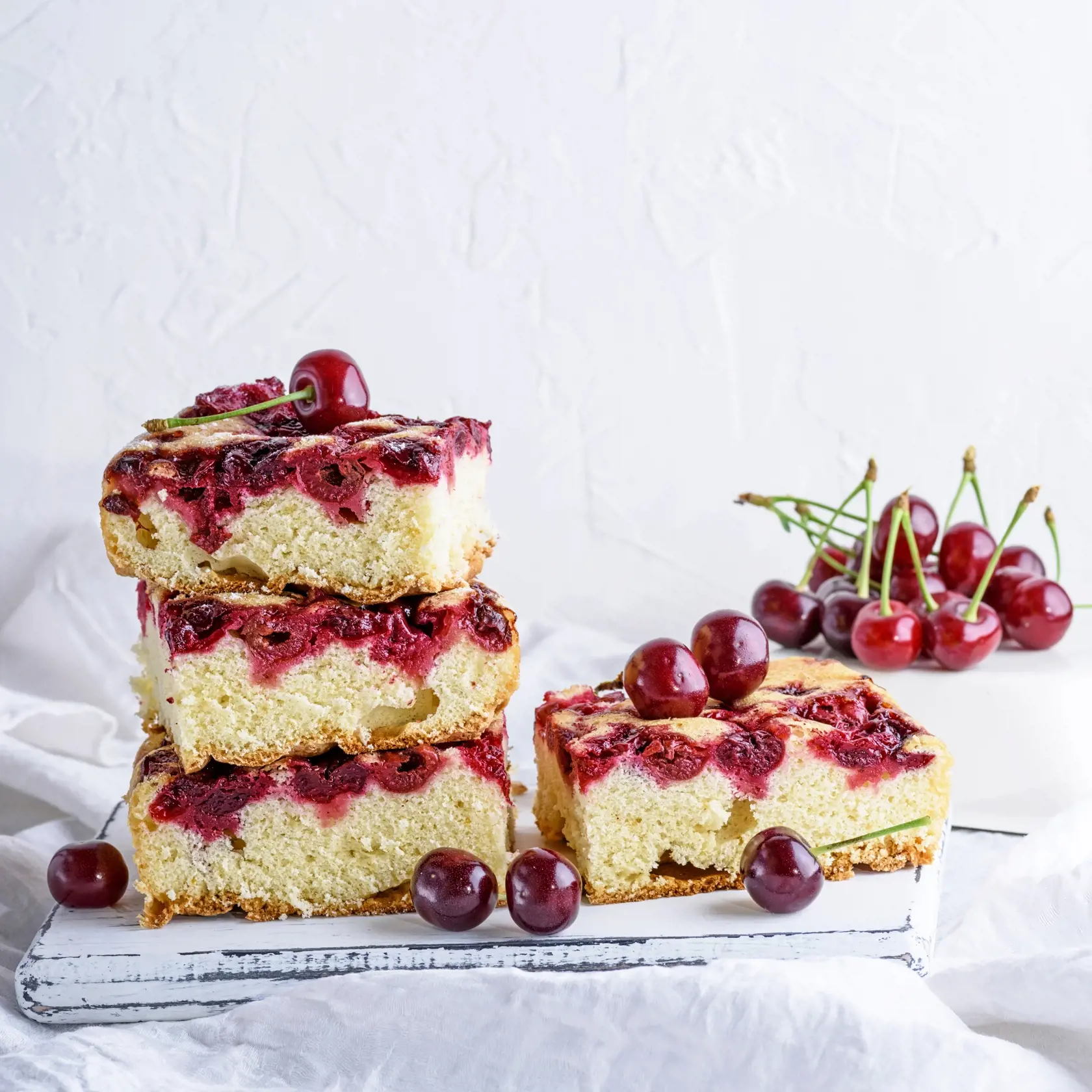 baked square pieces of a biscuit pie with cherries on a white wooden board, white background, copy space