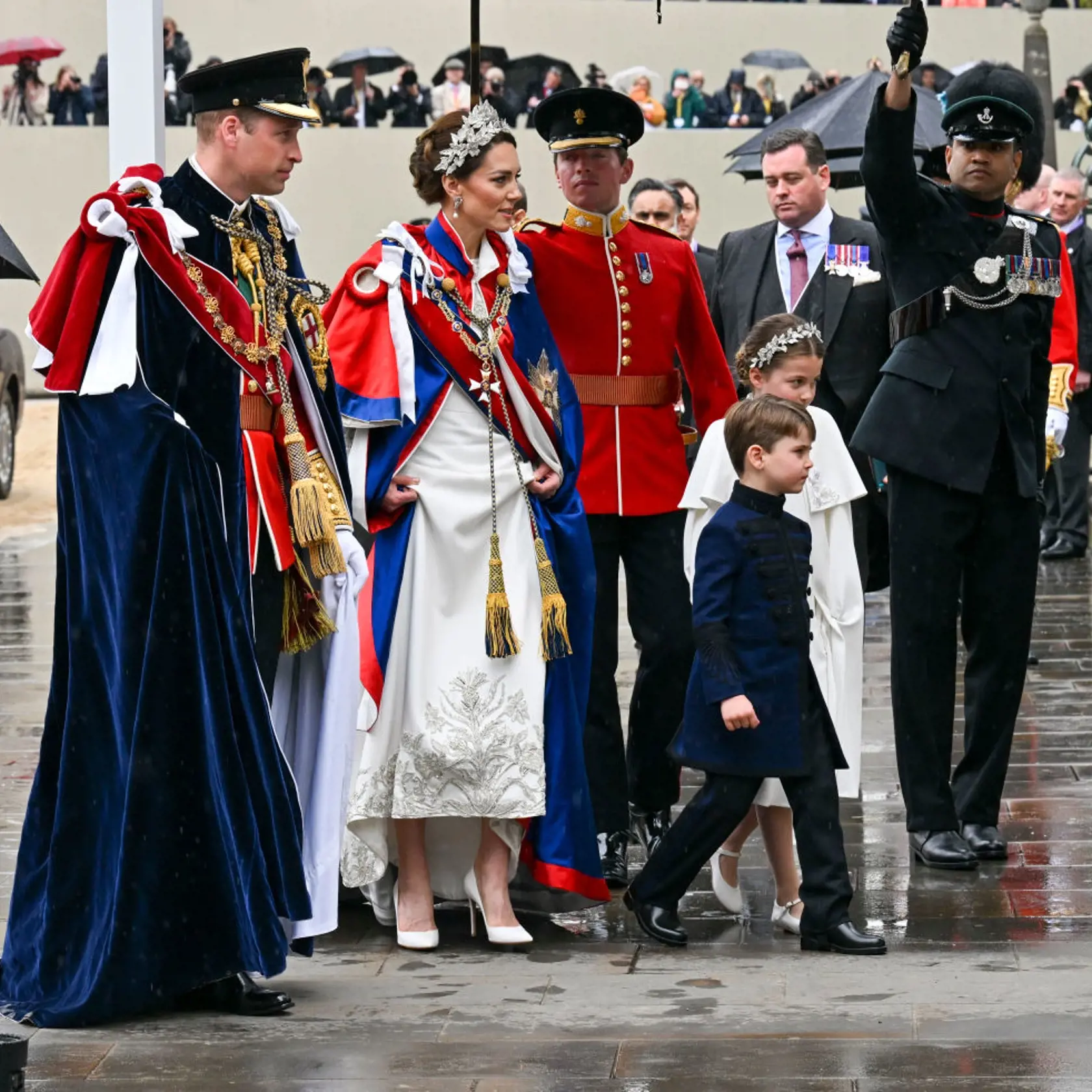 Princezná Kate mala na sebe tradičný ceremoniálny plášť. Pod ním slonovinové šaty od Alexandra McQueena a 3D čelenku, rovnako tak aj jej dcéra, princezná Charlotte.