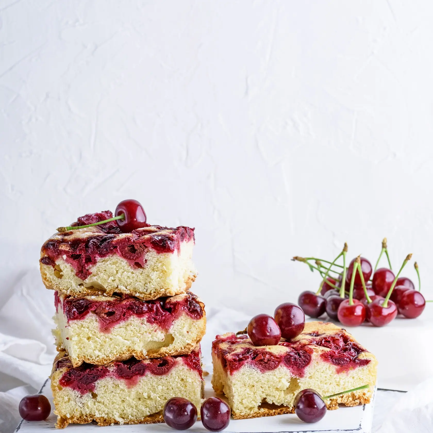 baked square pieces of a biscuit pie with cherries on a white wooden board, white background, copy space