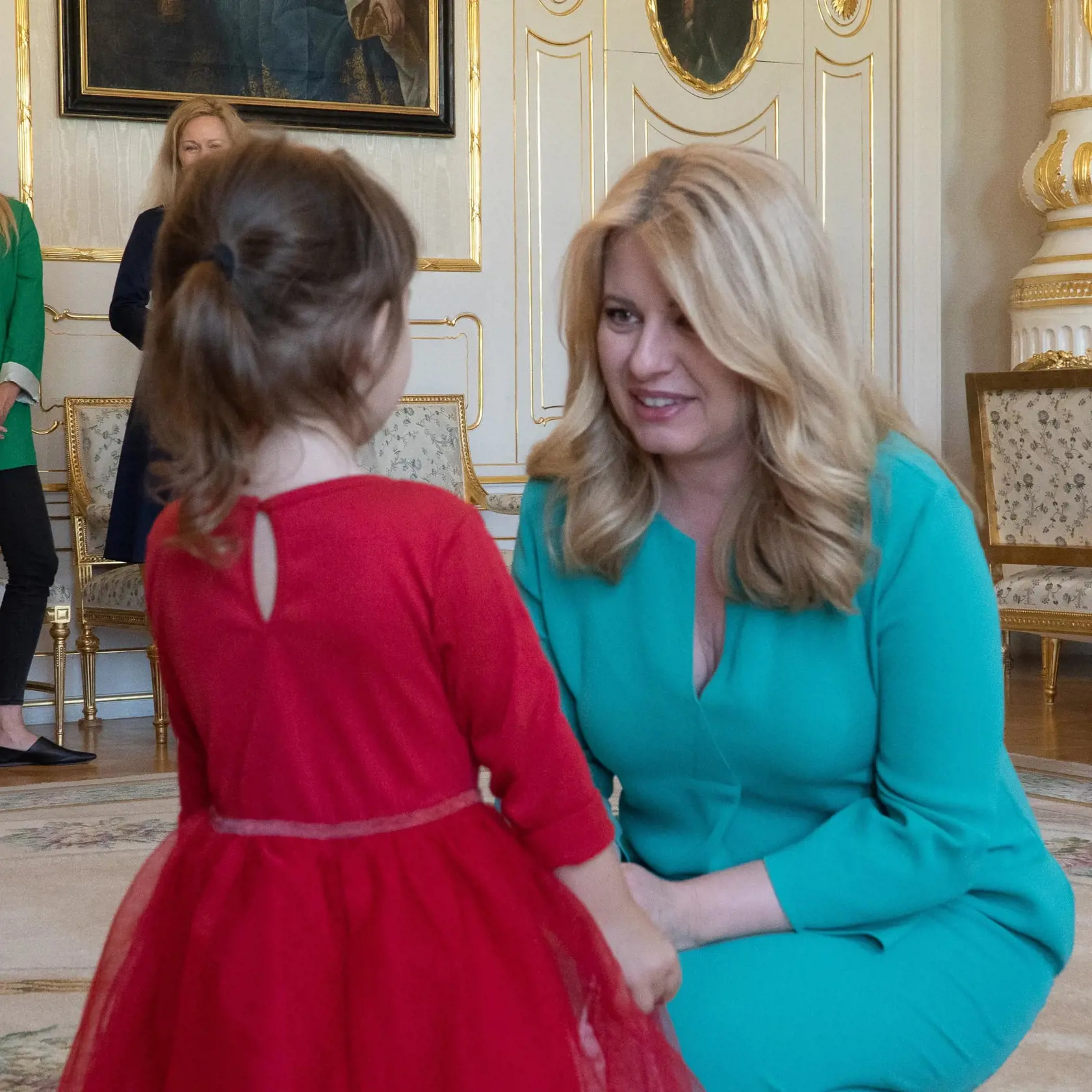 Upretý pohľad hostiteľky (Prezidentský palác) a malej návštevníčky. Vyzerá to tak, že Zuzana Čaputová počúva básničku alebo len pár milých slov ako pozdrav od dievčatka v červených šatôčkách.