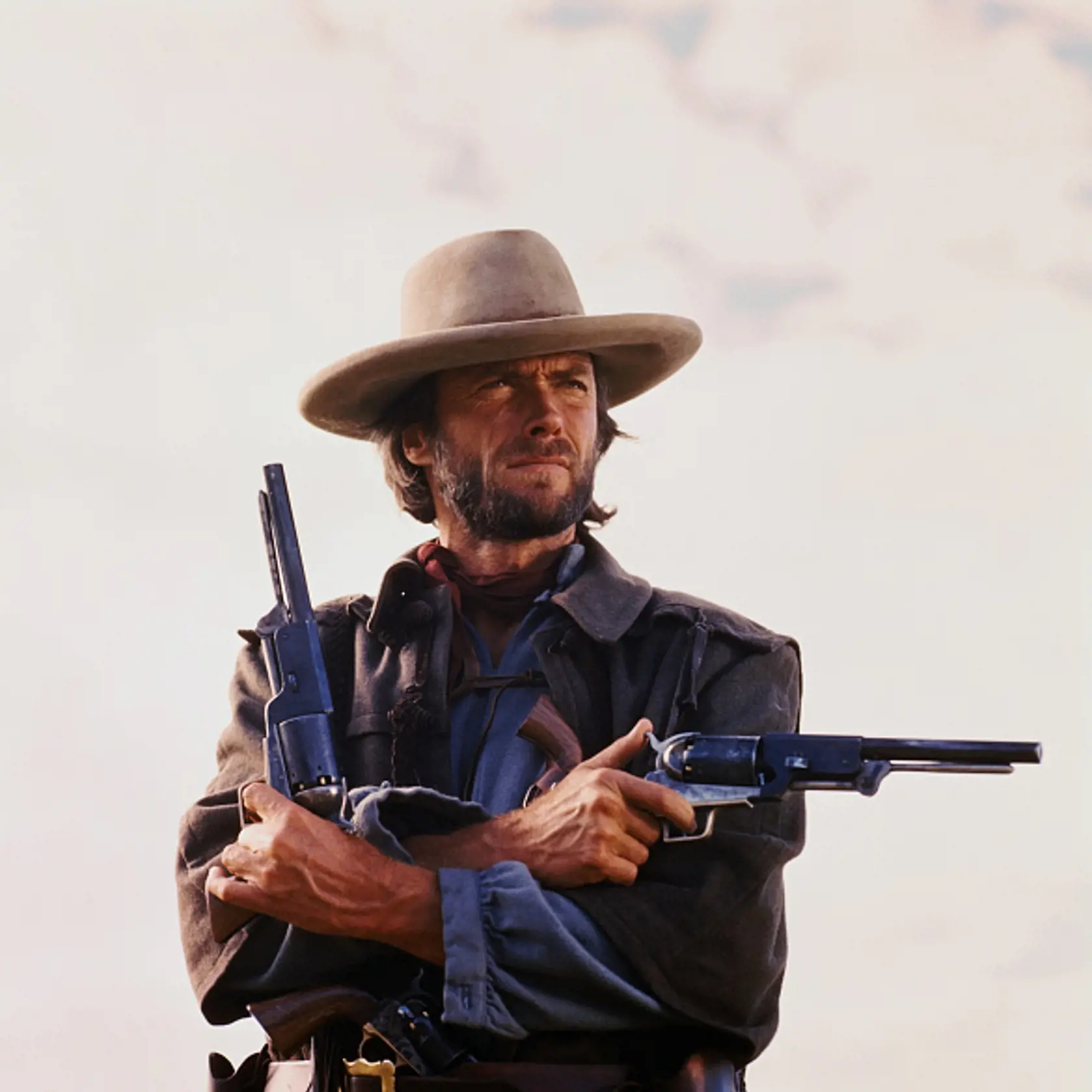 (Original Caption) Movie still of Clint Eastwood starring in the 1976 Western The Outlaw Josey Wales, directed by Clint Eastwood himself. Photo shows him from the waist-up holding two pistols, one pointing to his left and one pointing up, arms crossed.