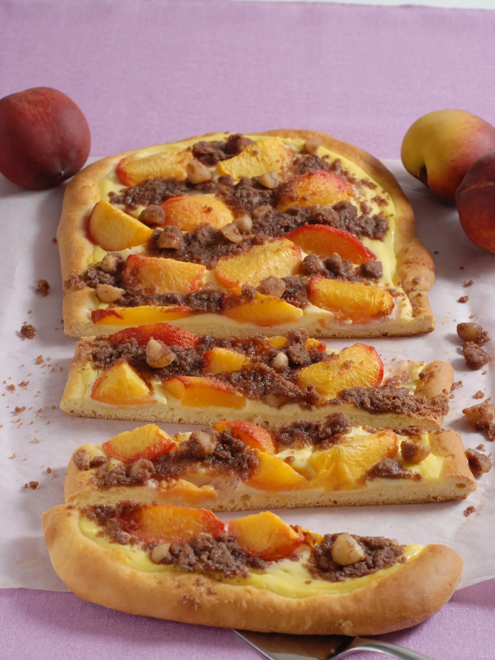 Broskyňová focaccia s ricottovým krémom
pre 10 osôb

Potrebujeme:
150 ml mlieka
20 g čerstvého droždia
90 g masla
350 g polohrubej múky 
120 g jemného kryštálového cukru
2 vajcia
60 g makadamových orieškov
2,5 lyžičky kakaa
250 g ricotty
nastrúhanú citrónovú kôru
1 balíček vanilínového cukru
450 g broskýň


Postup:
1 V kastróliku mierne zohrejeme mlieko, do ktorého rozdrobíme droždie, a rozpustíme 50 g masla. 
Do misy preosejeme 290 g múky, pridáme 30 g cukru, 1 vajce, tekuté maslo a rozpustené 
