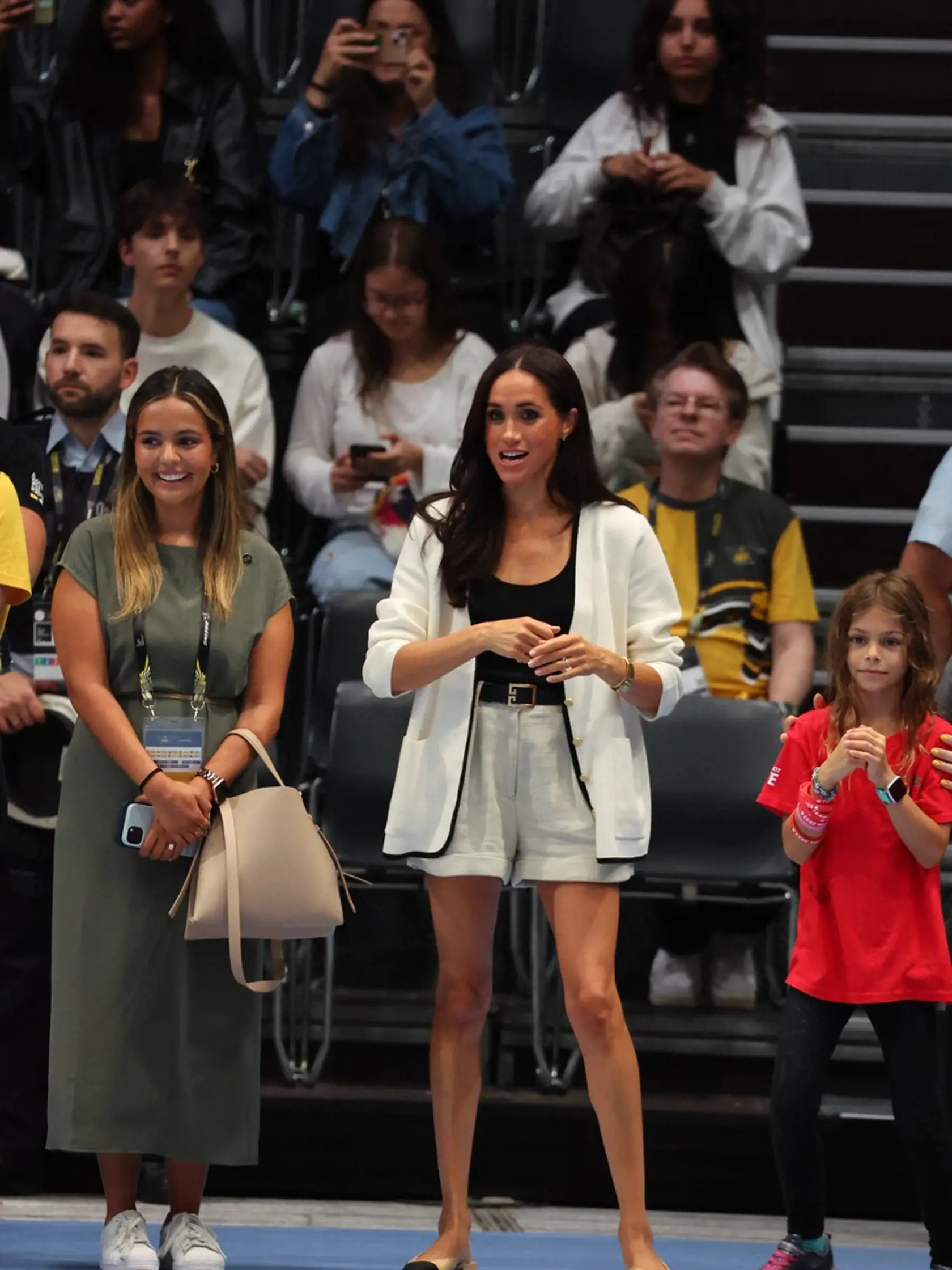 Na rozdiel od predchádzajúceho večera zvolila Meghan aj ležérnejší outfit. Štíhle nohy predviedla v krátkych elegantných šortkách doplnených o čierne tielko a biele sako.